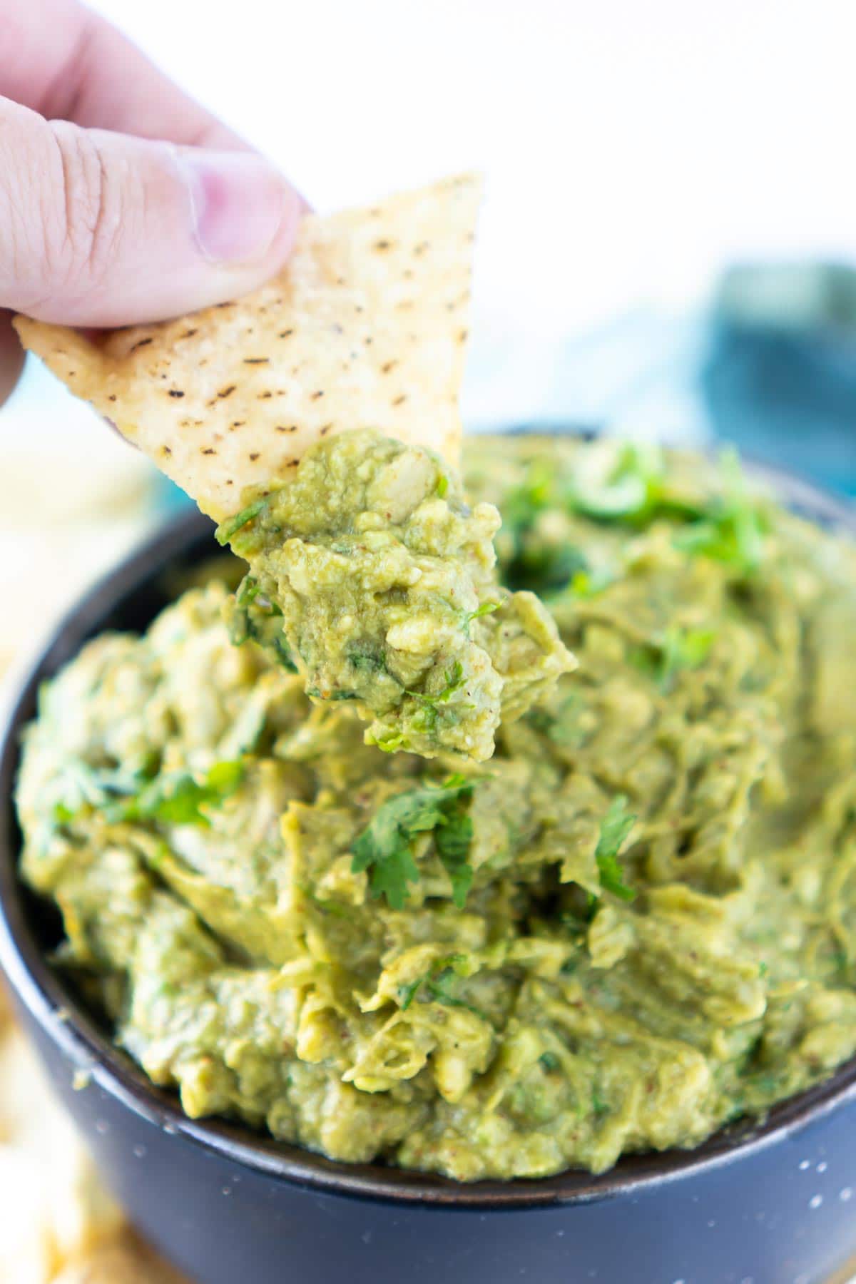 Woman's hand holding a tortilla chip above a bowl of guacamole