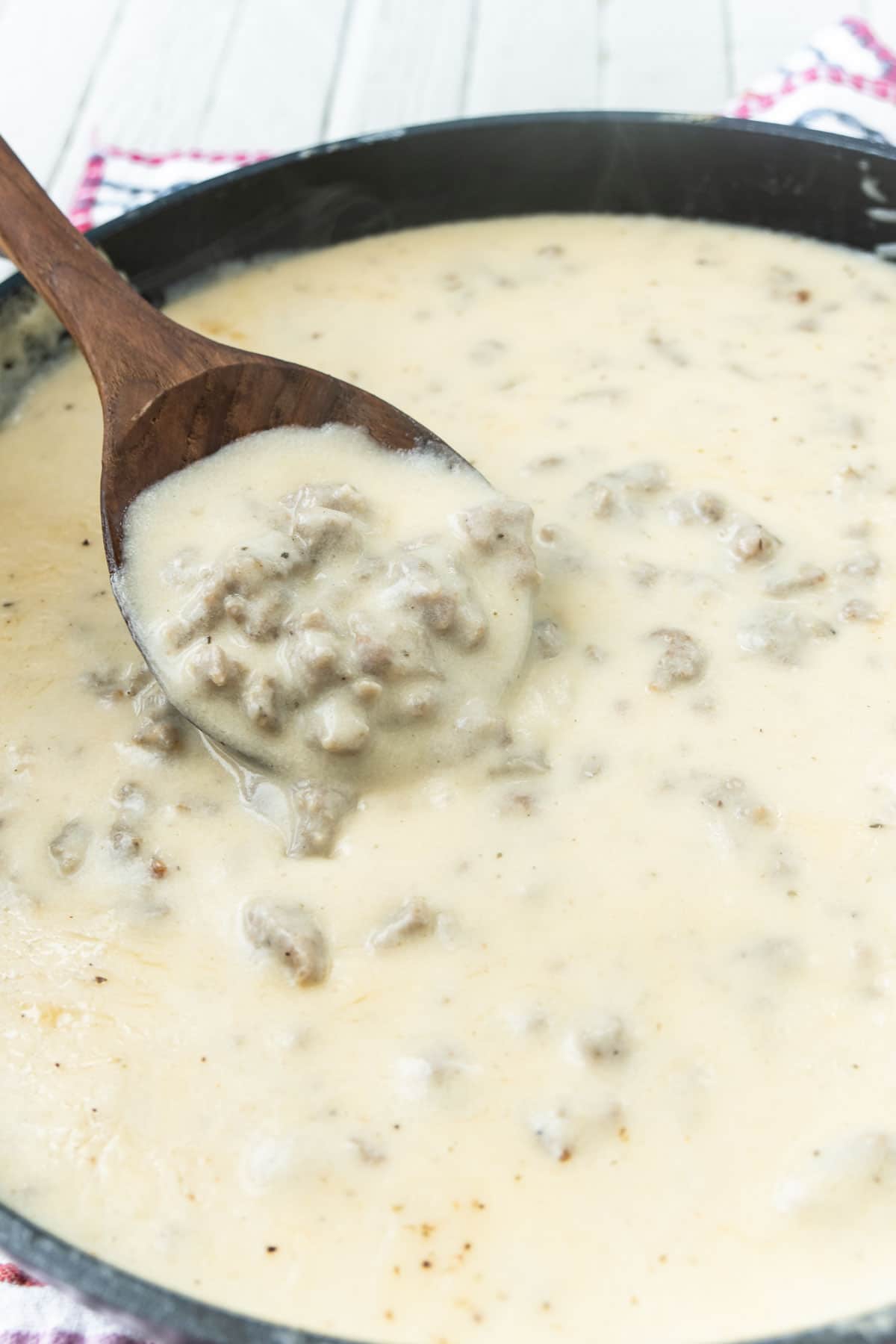 Pan of sausage gravy with a wood spoon