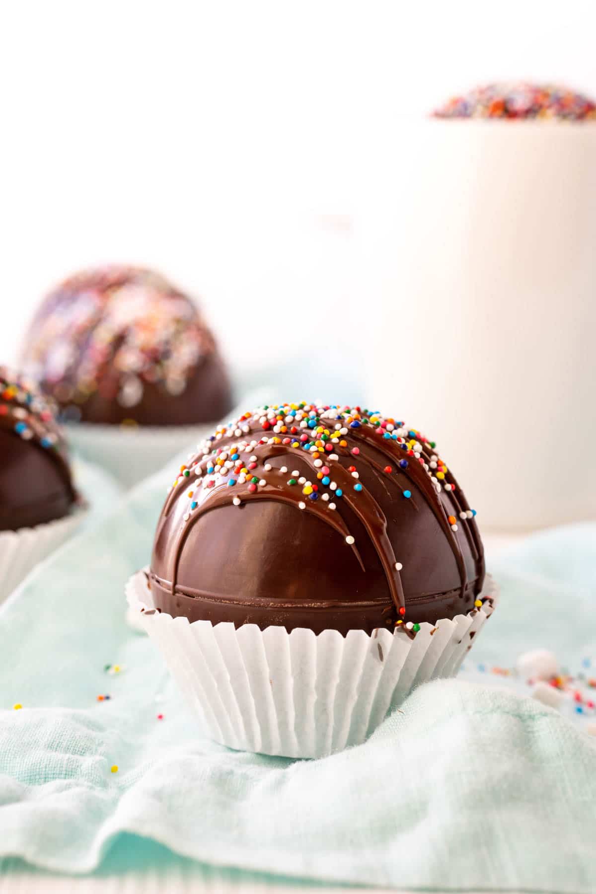 Hot chocolate bombs with sprinkles on top and a glass of milk in the background