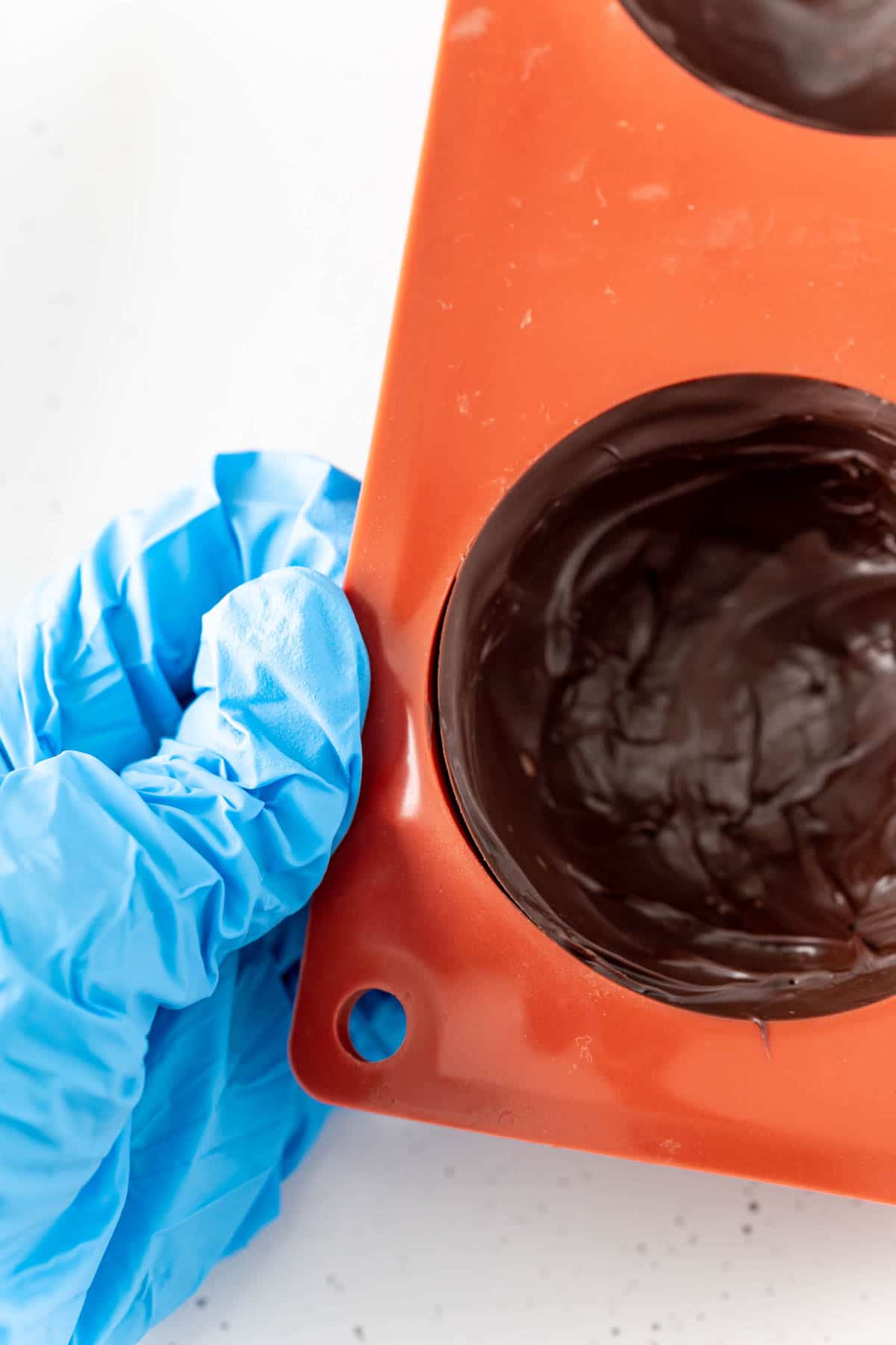 Woman's hand in a glove holding a hot chocolate bomb mold