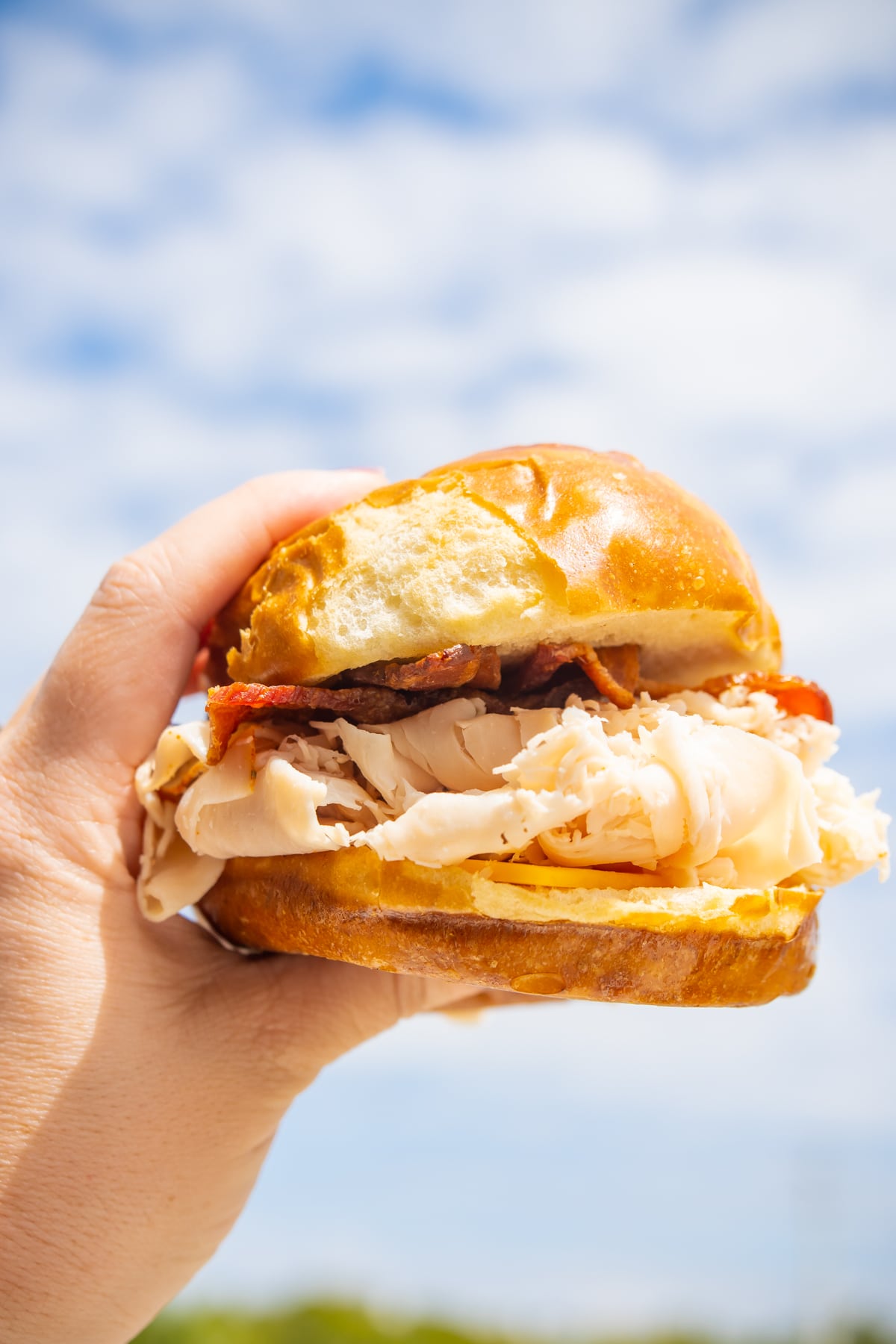 woman's hand holding a sandwich in front of the sky