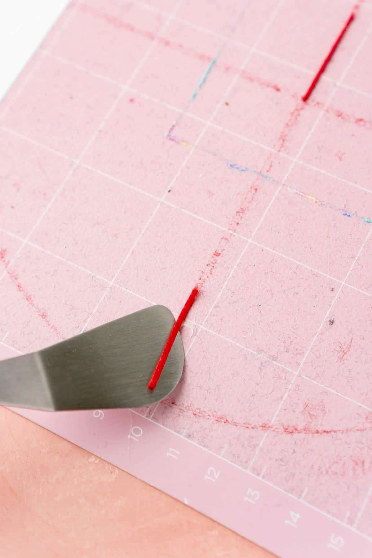 Cricut spatula scraping off excess felt from a pink mat
