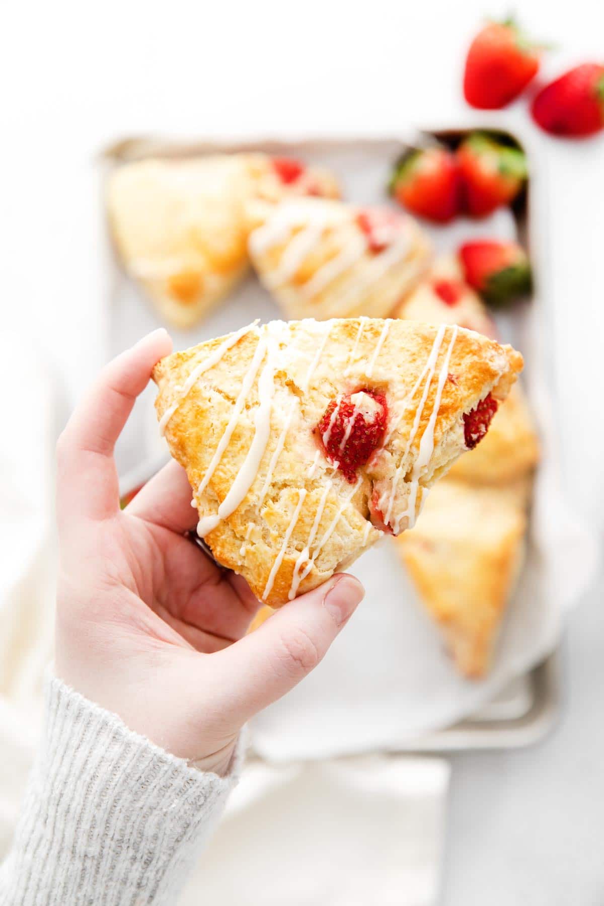 strawberry scone drizzled with vanilla frosting in someone's hand