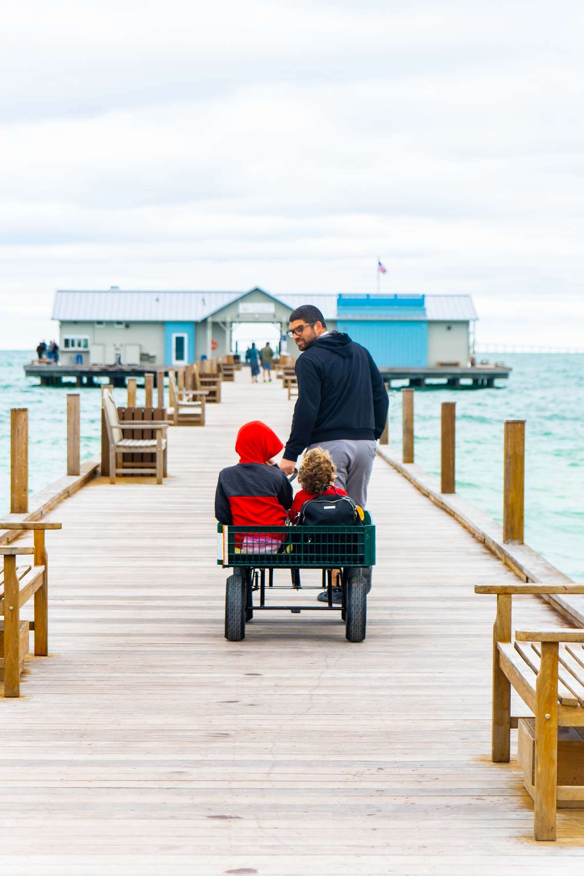 Man pulling a wagon with two boys on a wood pier