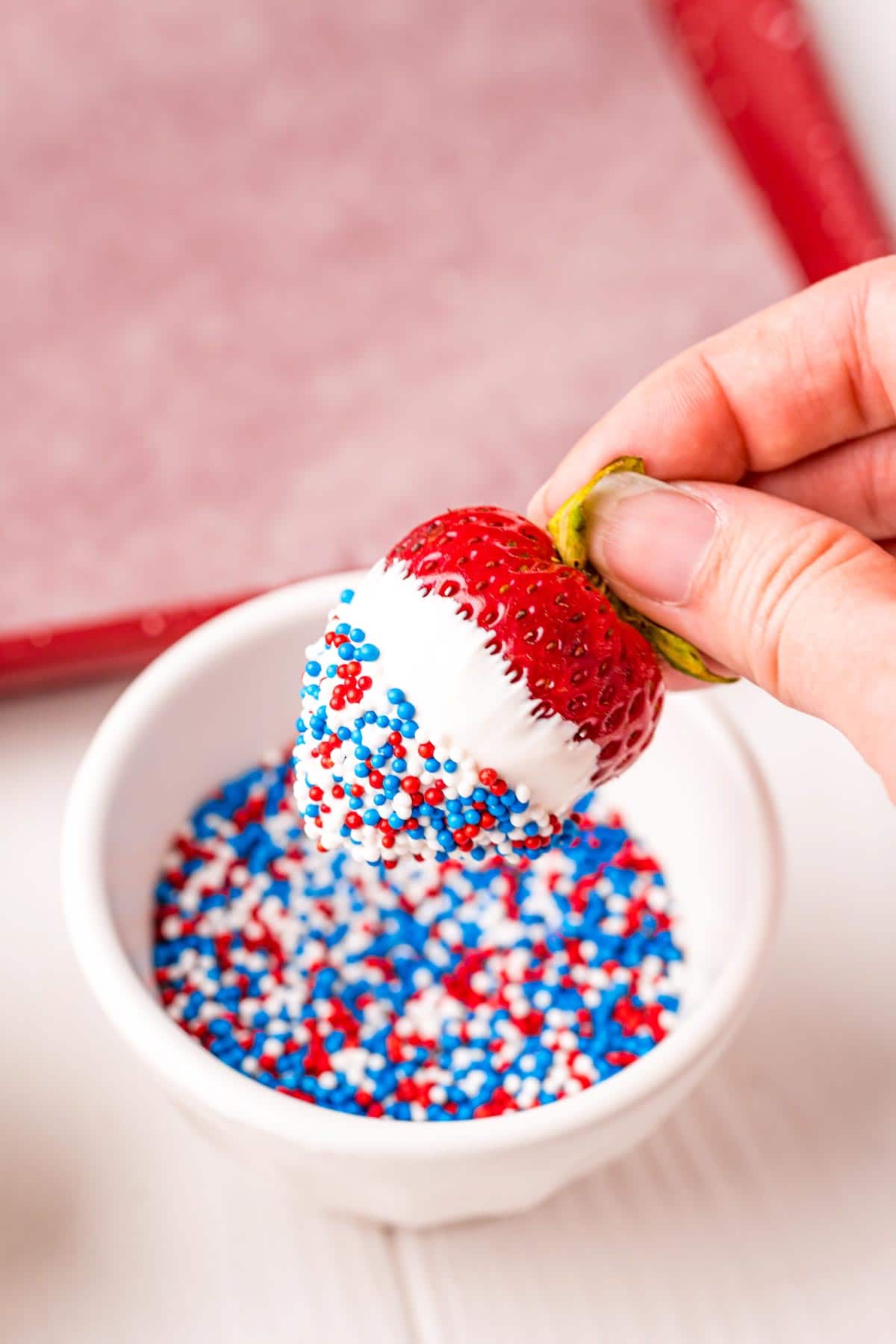 hand dipping a strawberry in sprinkles