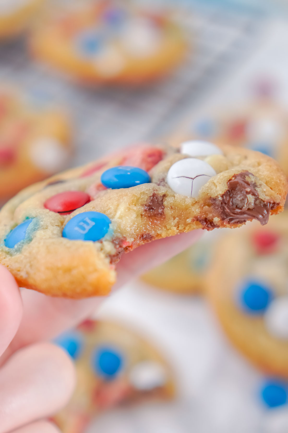 hand holding a chocolate chip M&M cookie with a bite out of it