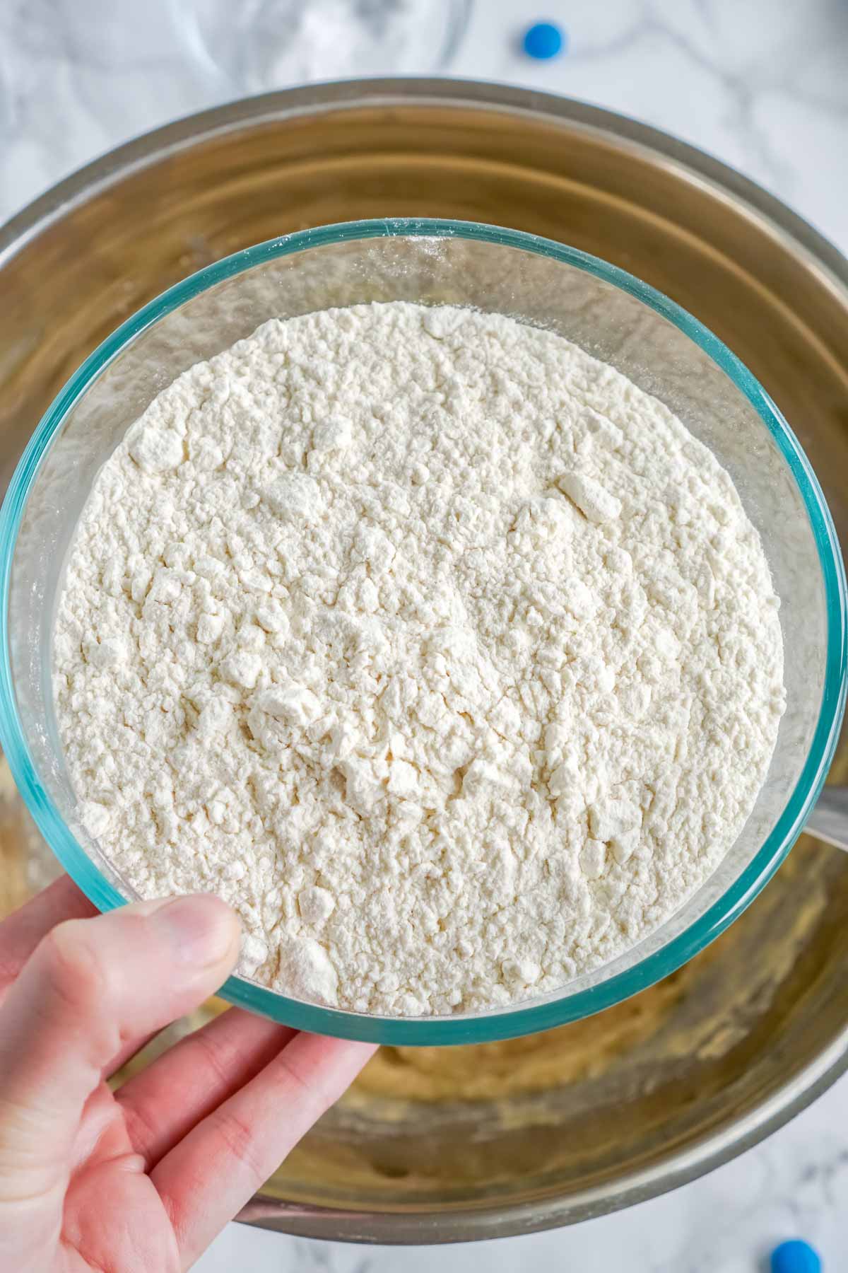 hand holding a bowl of flour above cookie dough