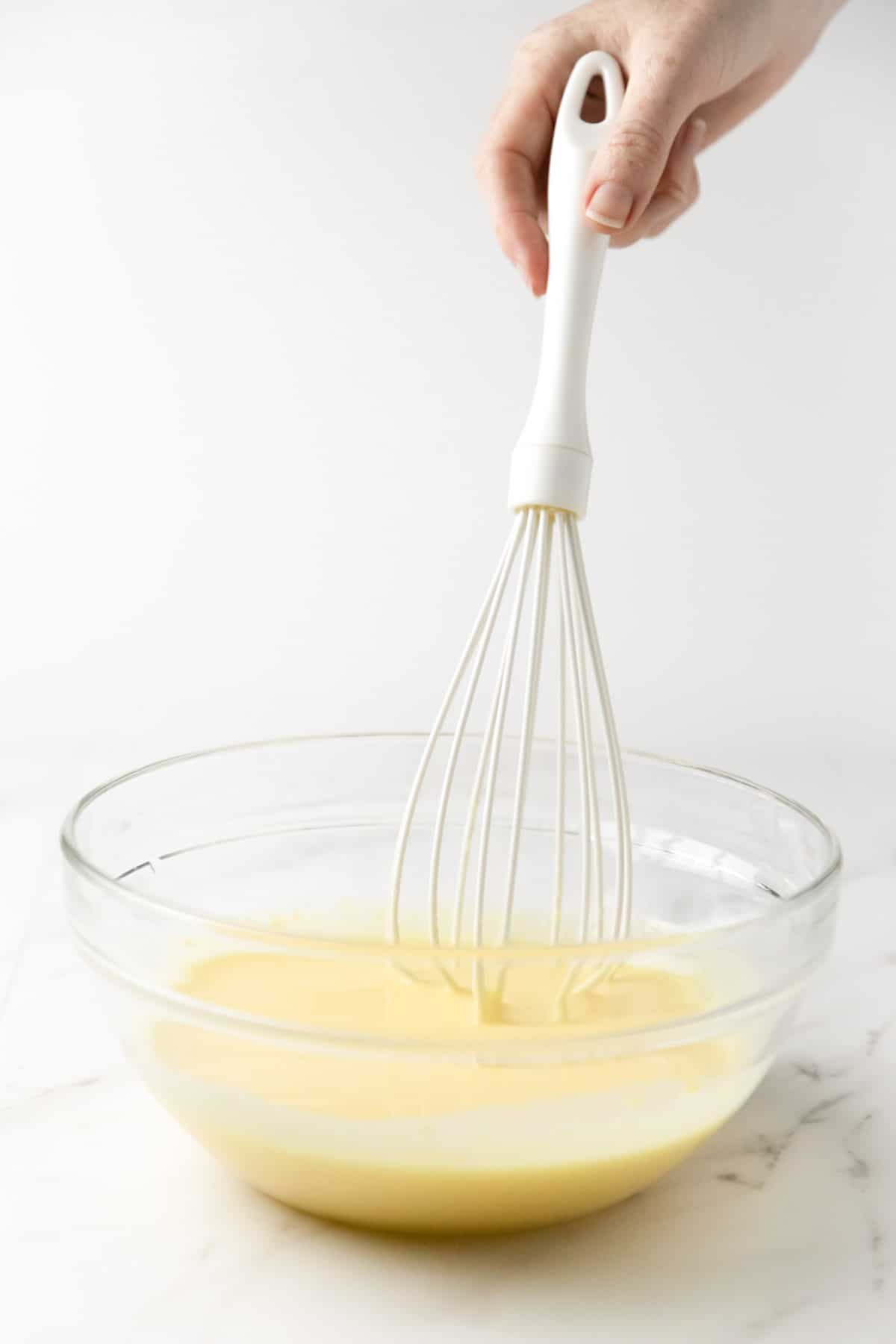 whisk held by a hand mixing vanilla pudding