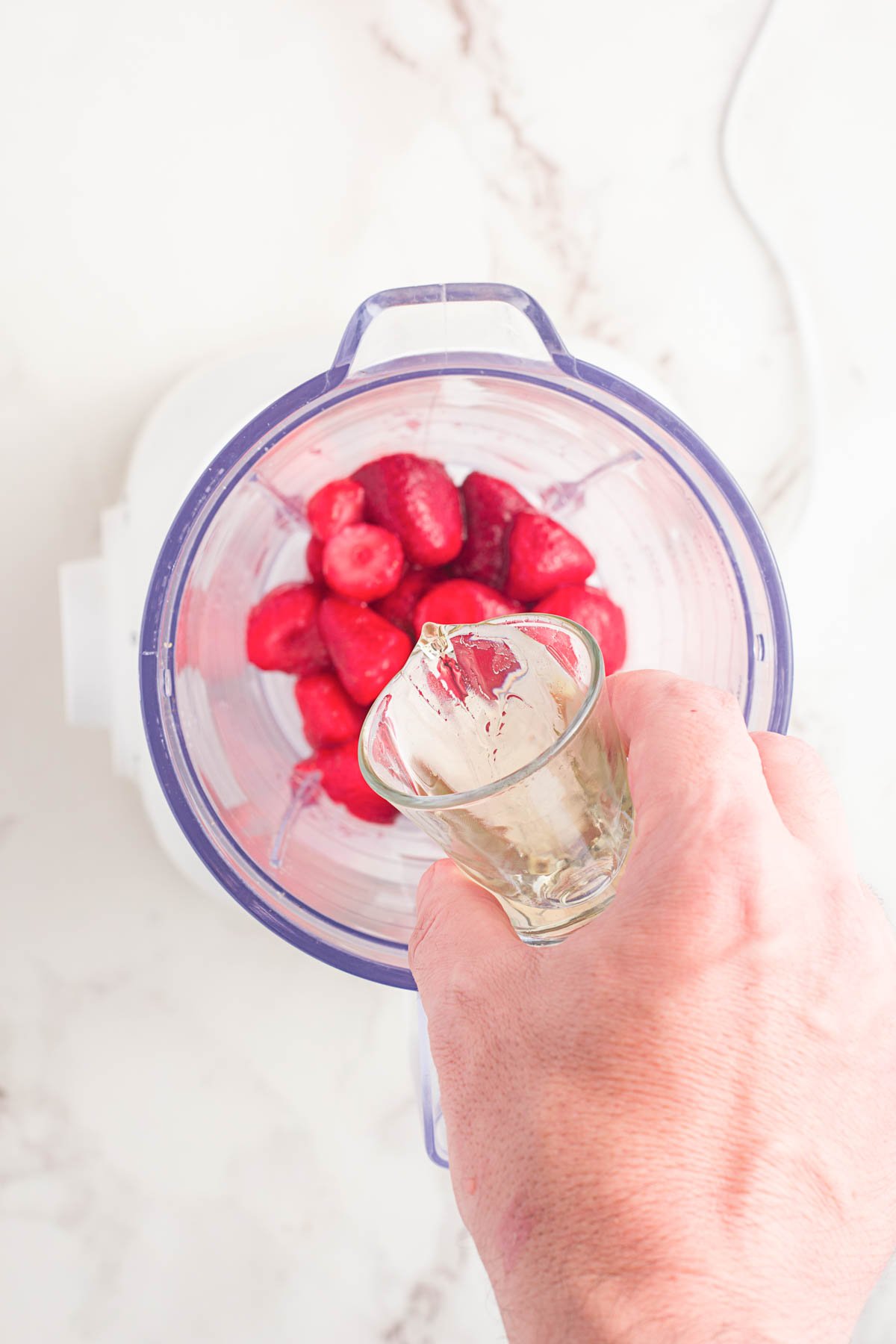 hand pouring simple syrup into a blender