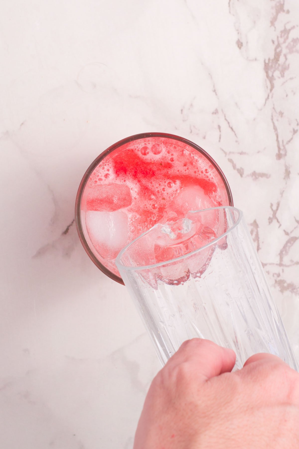 pouring ice into a glass of strawberry lemonade