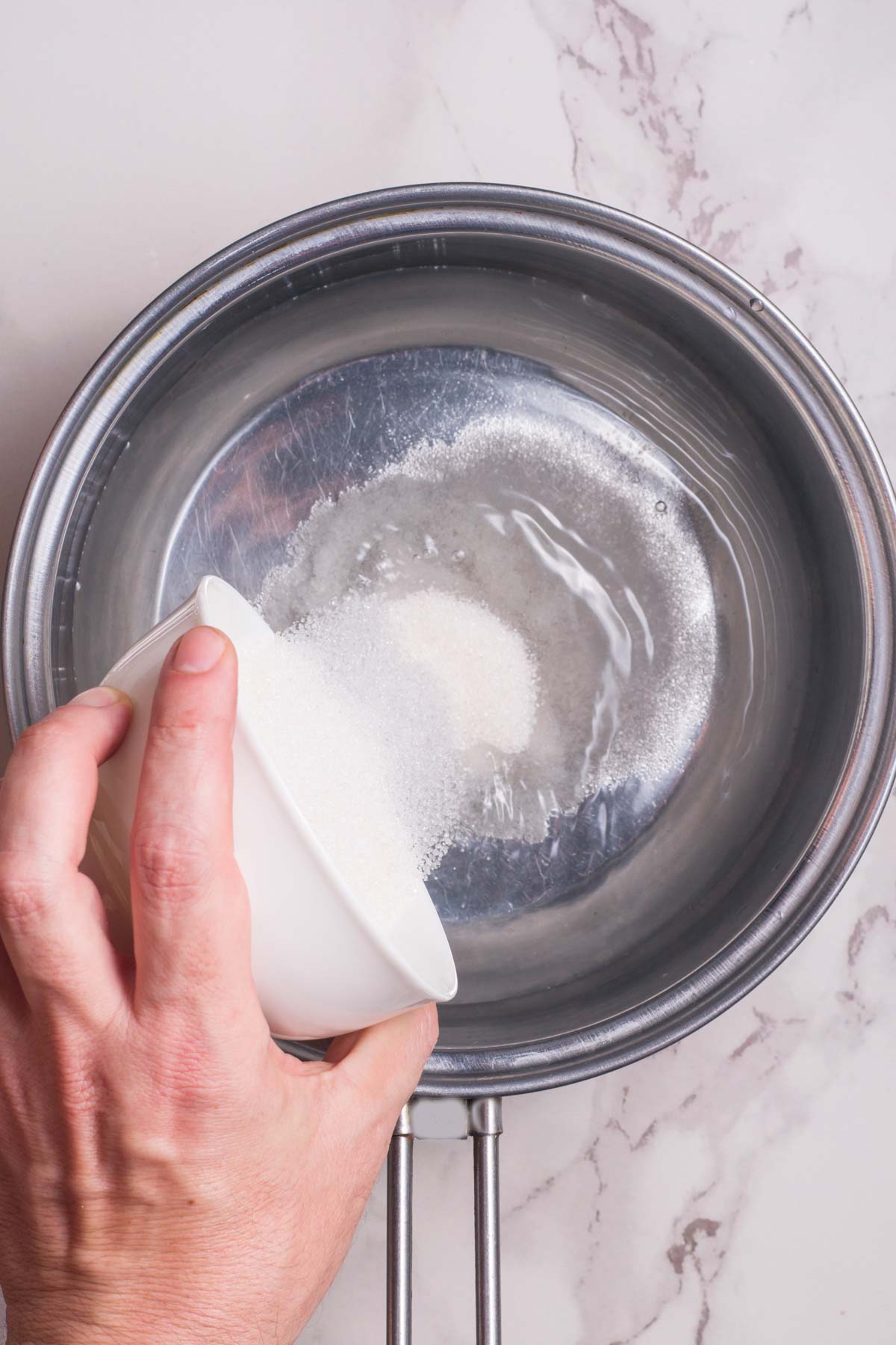 hand pouring sugar in a pan of water