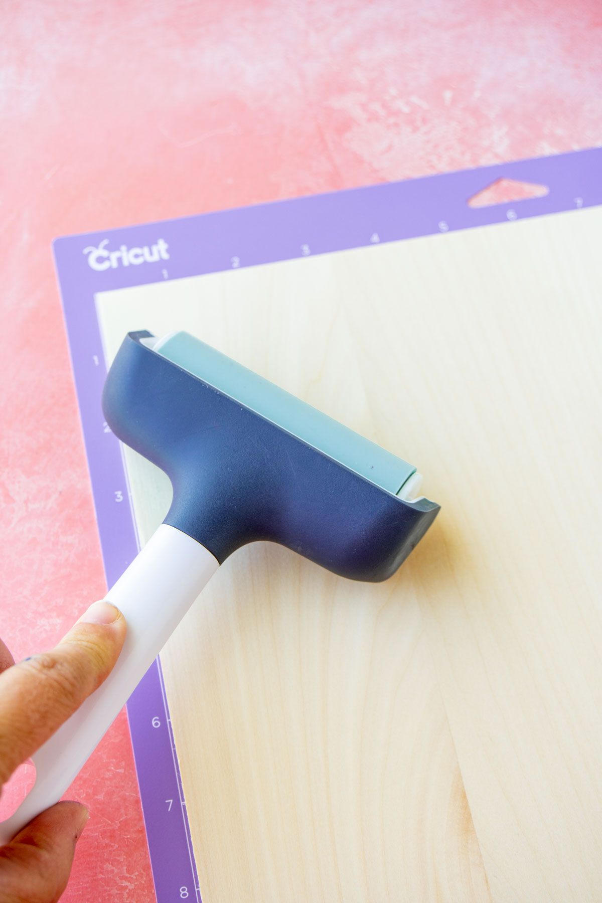 hand holding a Cricut brayer pressing down wood on a mat