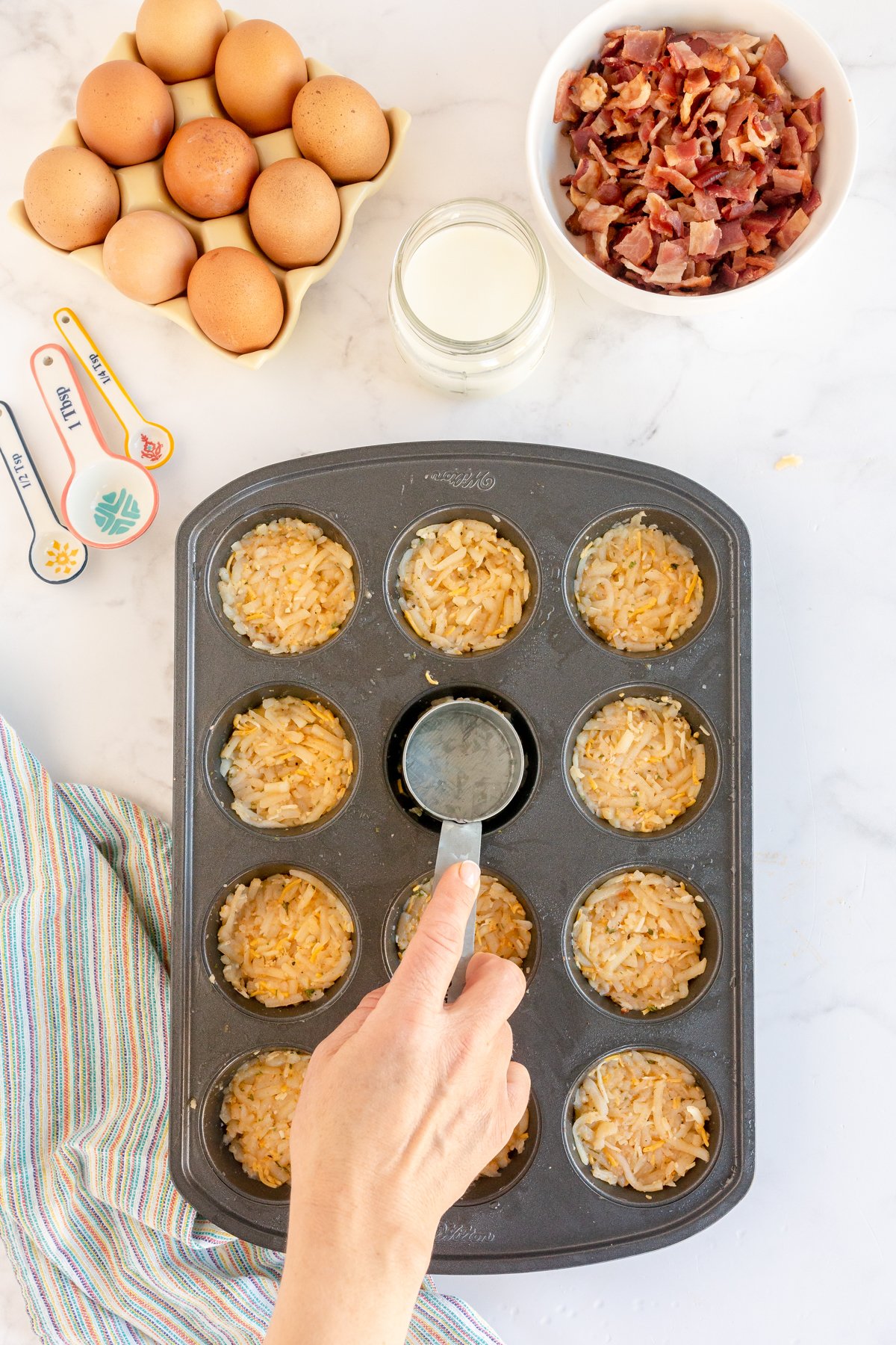 hand pressing hash browns into muffin tins