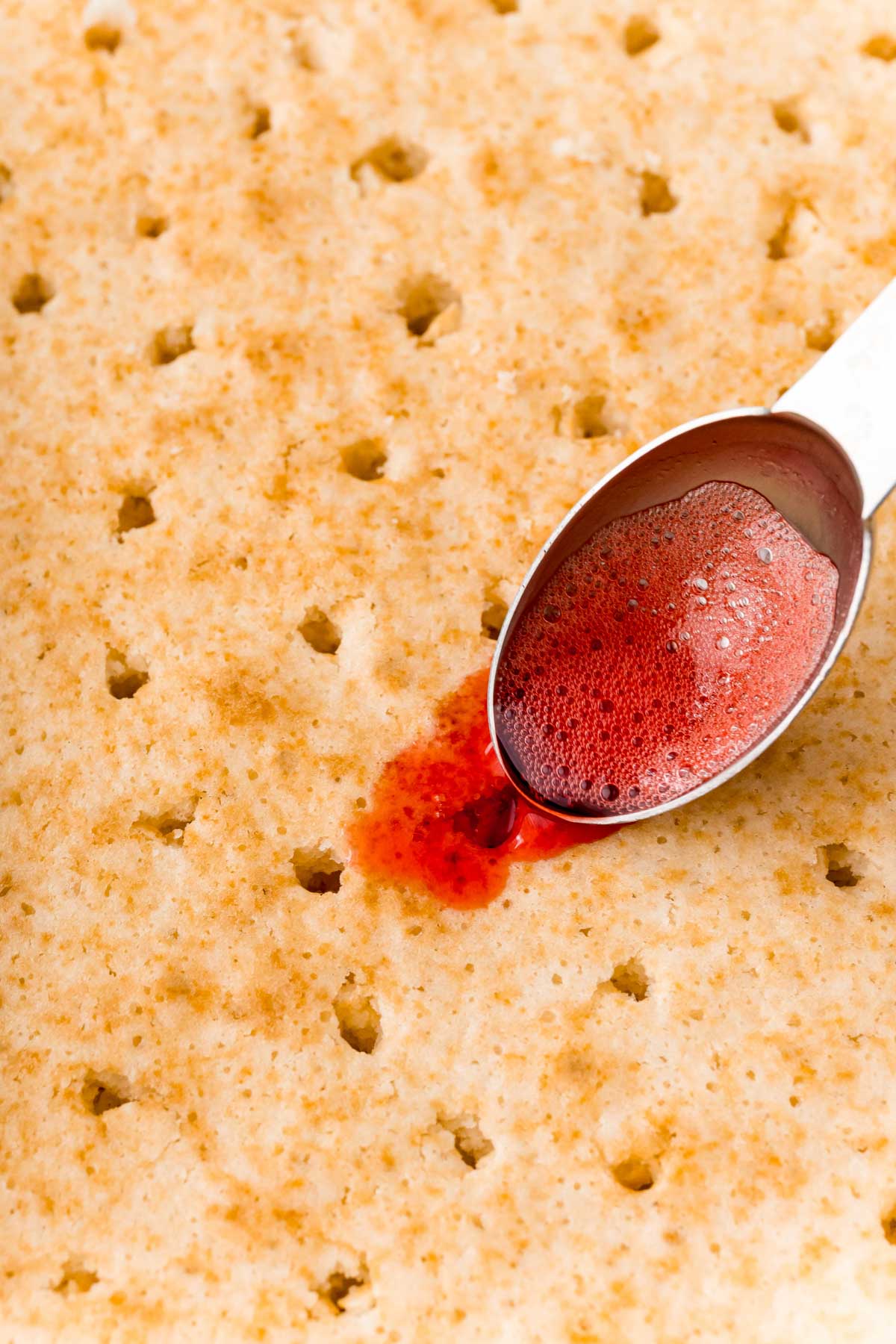 spoon pouring red jello mixture over cake