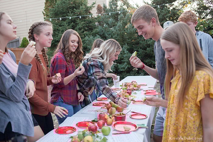 people grabbing apples off of a table outside