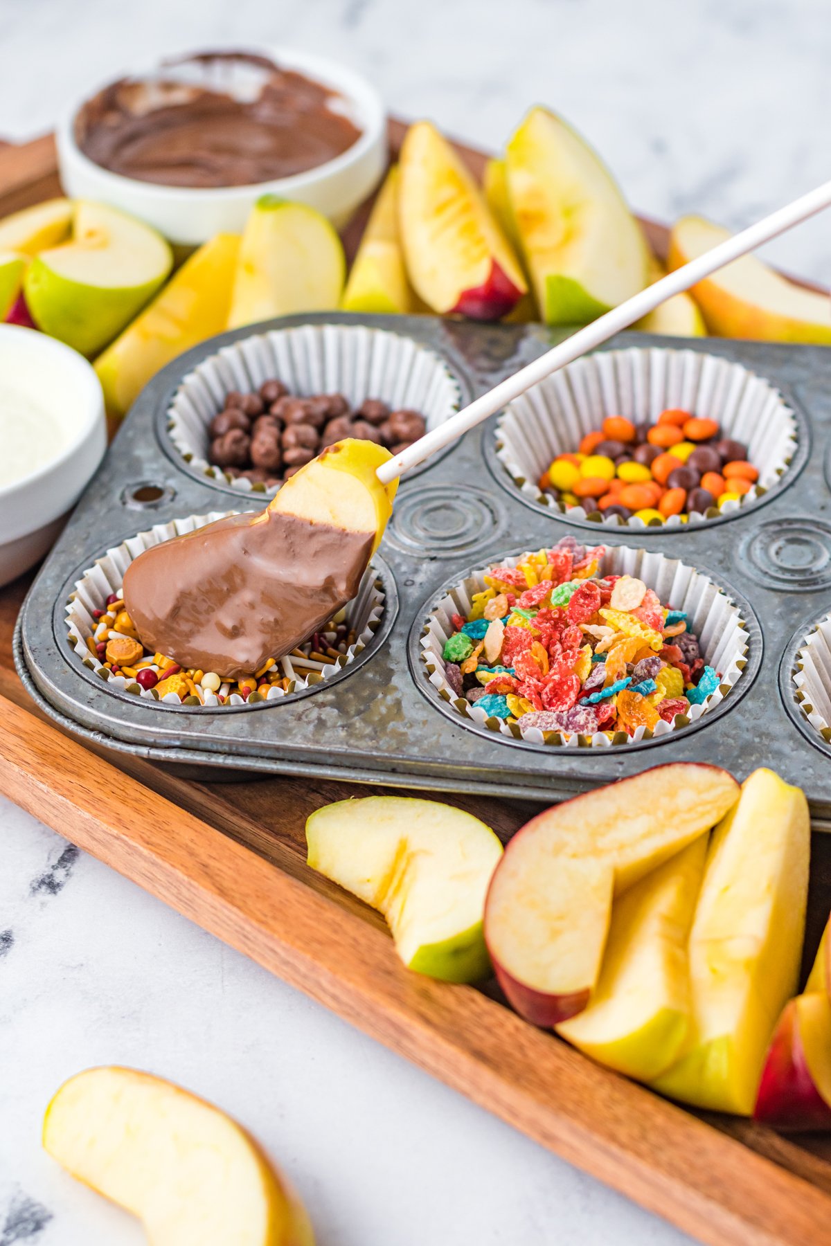 apple covered in chocolate being dipped in toppings