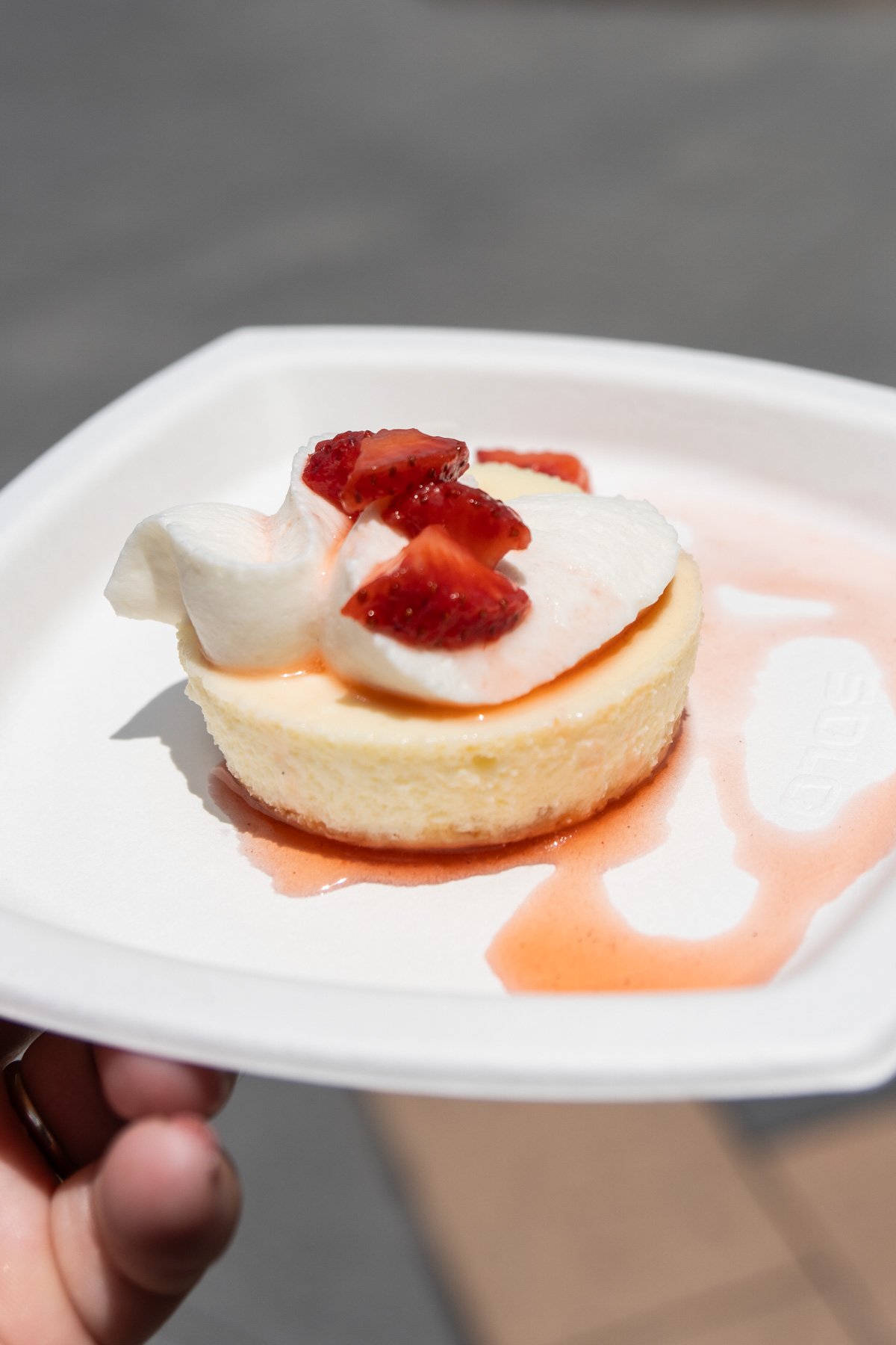 hand holding a white plate with a piece of lemon cheesecake