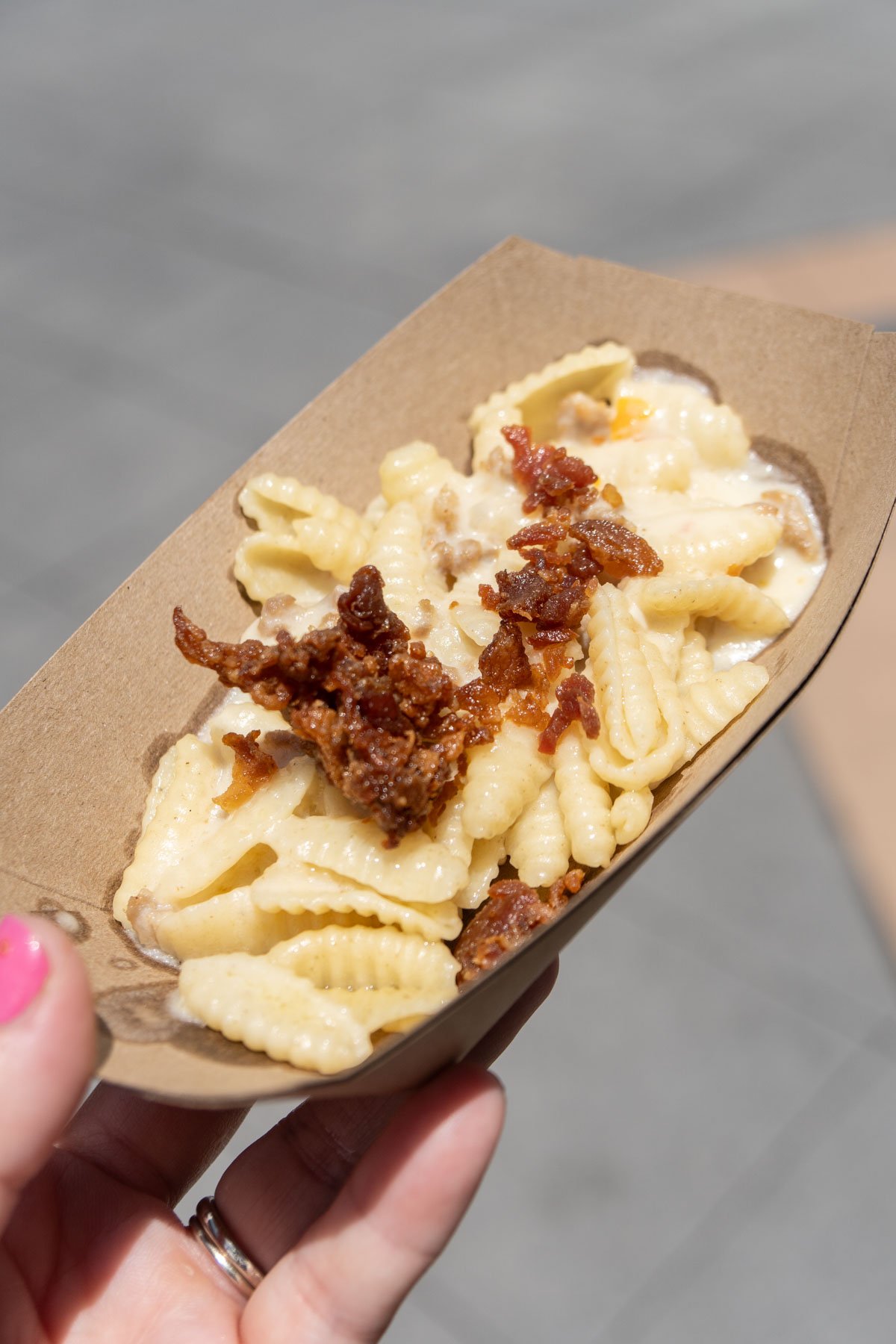 hand holding a cardboard boat with sausage pasta in it