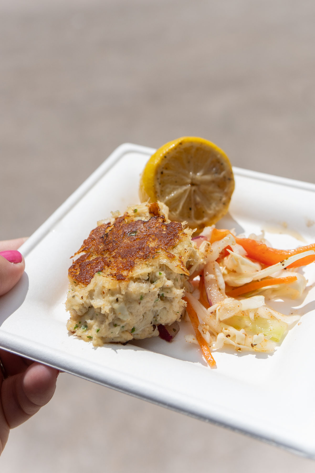 hand holding a white plate with a mushy crab cake