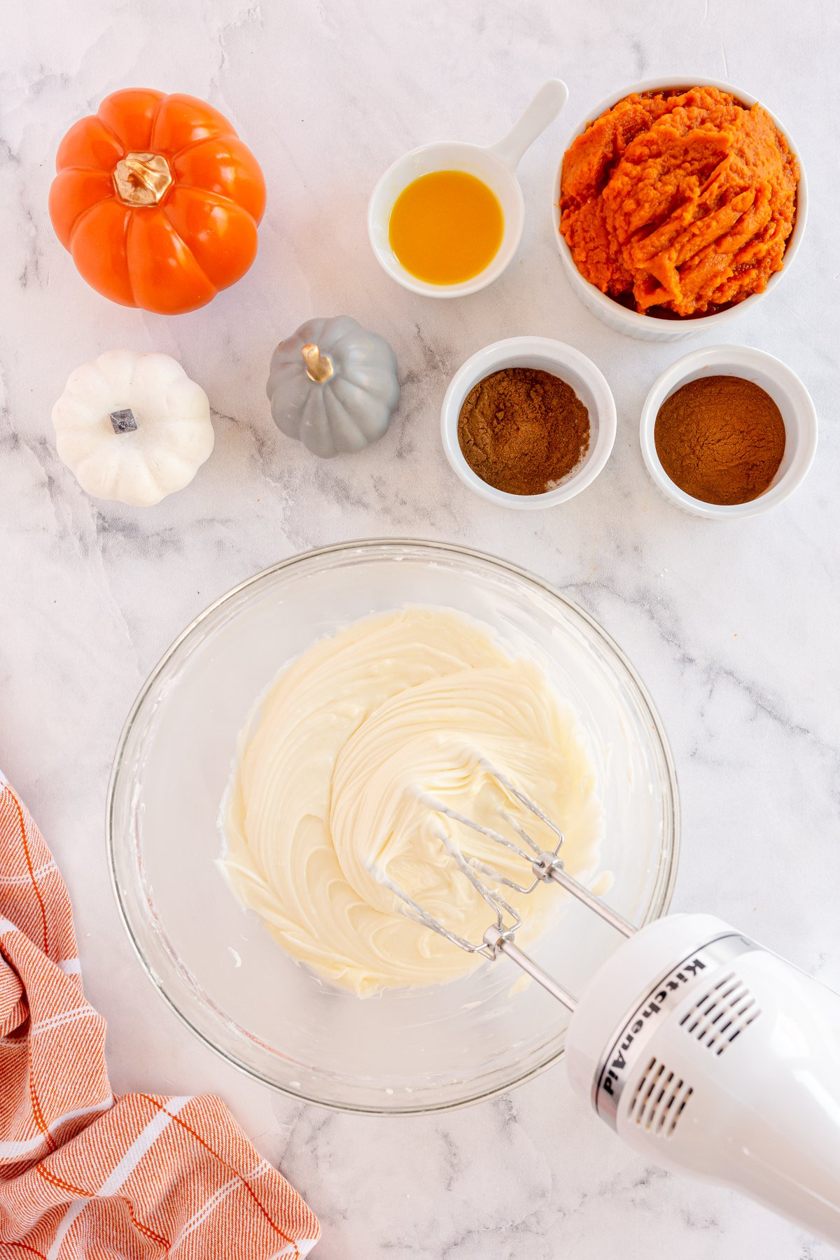 hand mixer beating cream cheese in a glass bowl