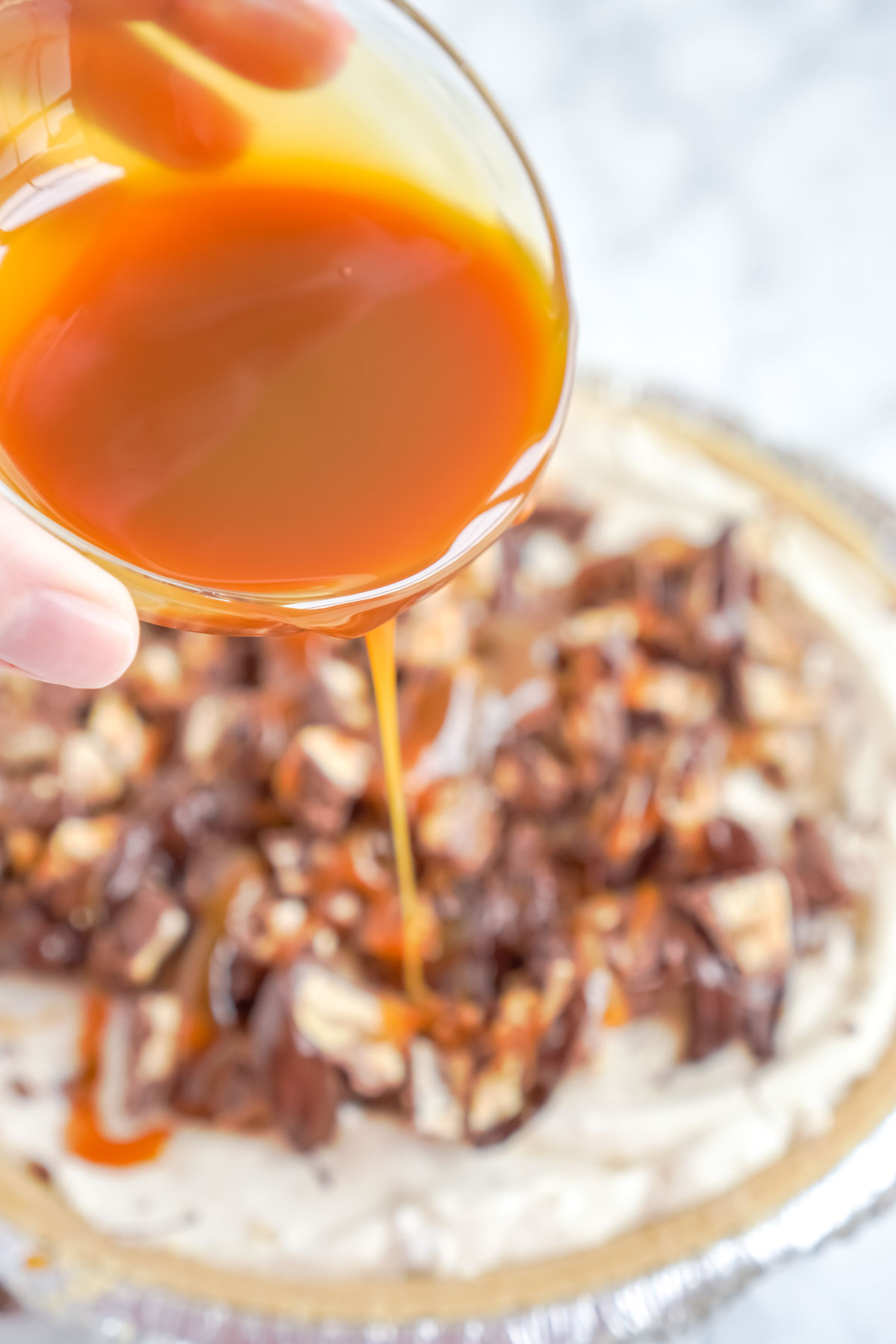 hand pouring caramel on snickers pie