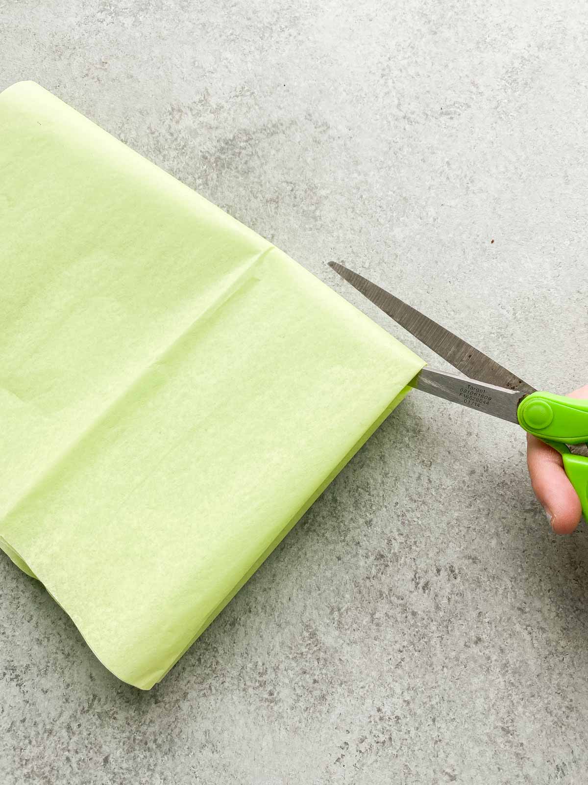 Scissors cutting green tissue paper in squares