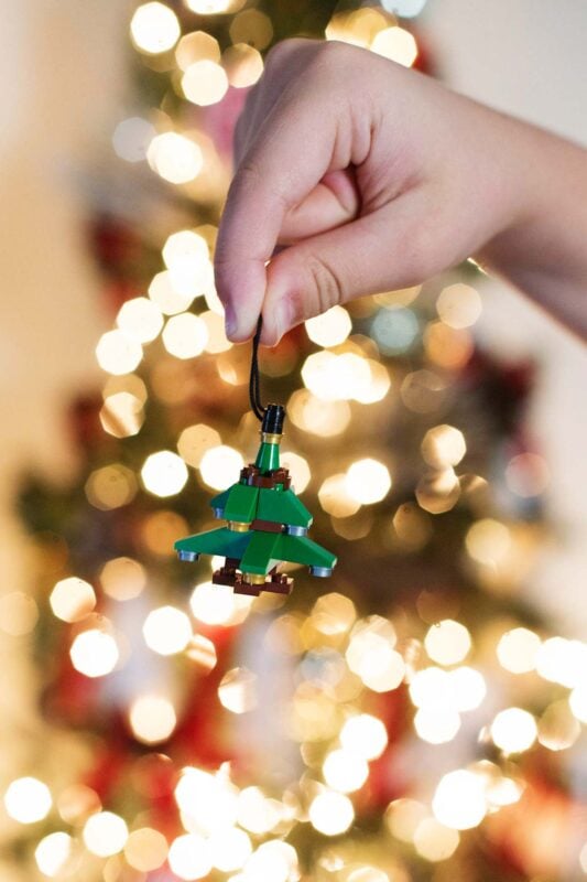 hand holding a Lego ornament in front of lights