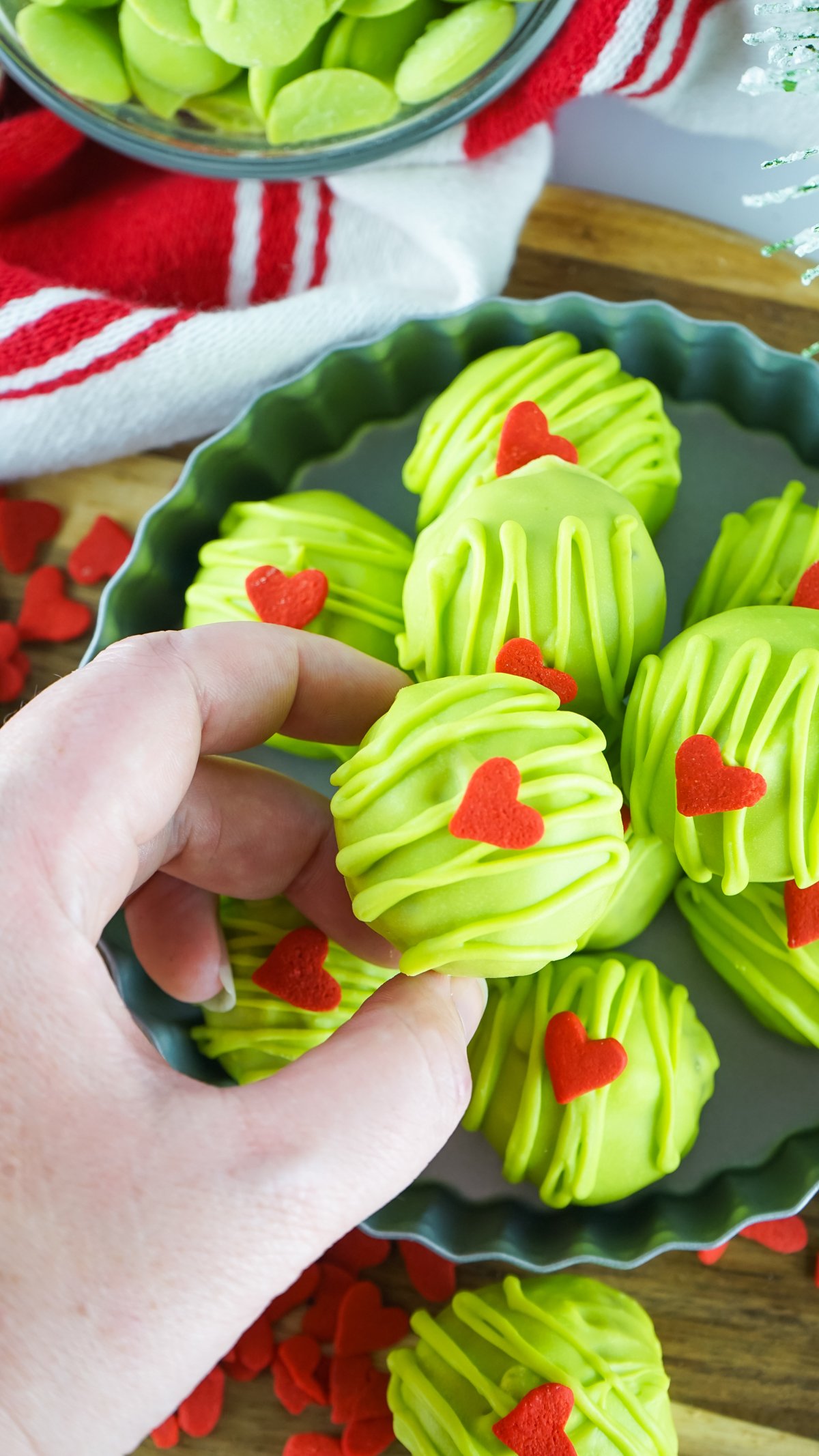 hand holding a Grinch Christmas ball above a plate full