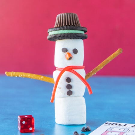 Marshmallow snowman standing next to a die
