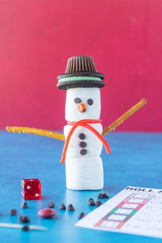 Marshmallow snowman standing next to a die