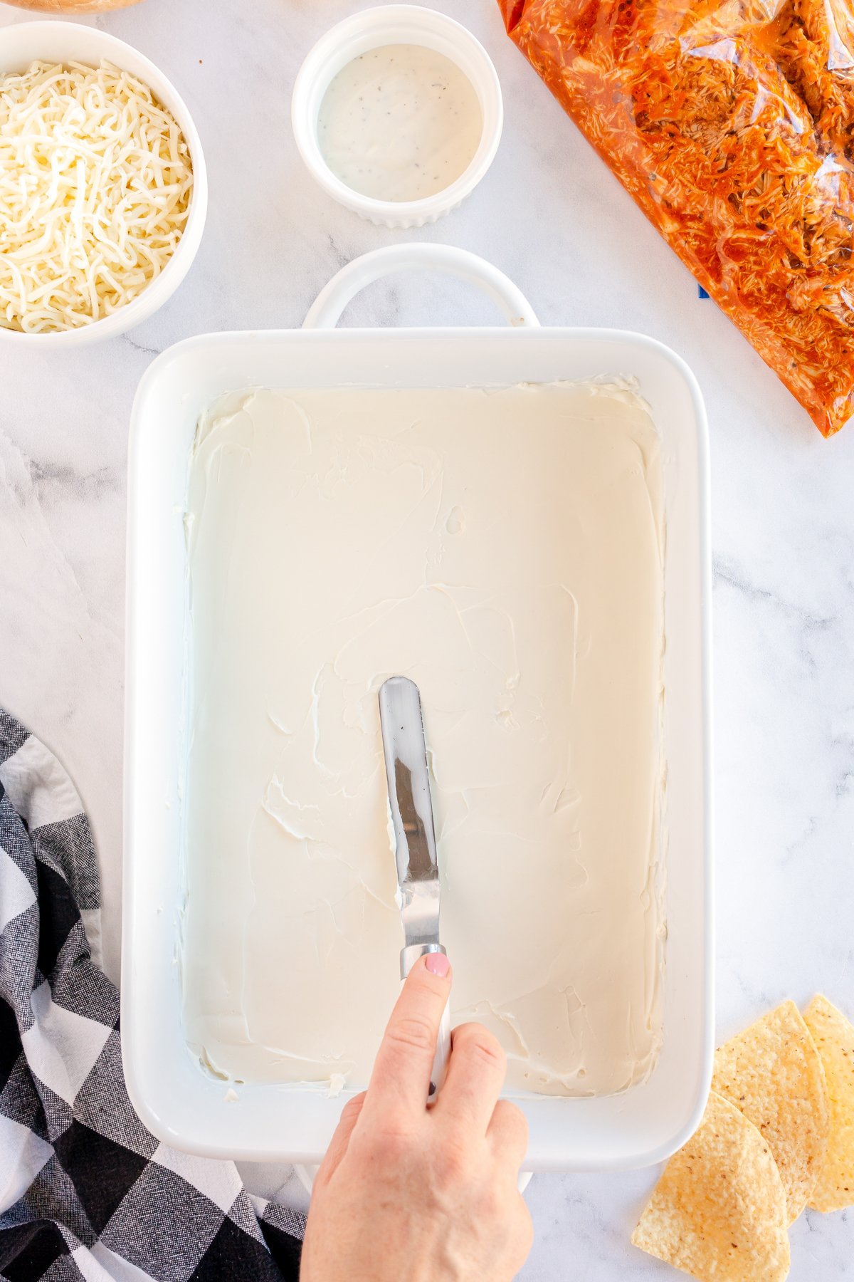 hand spreading cream cheese in a baking pan