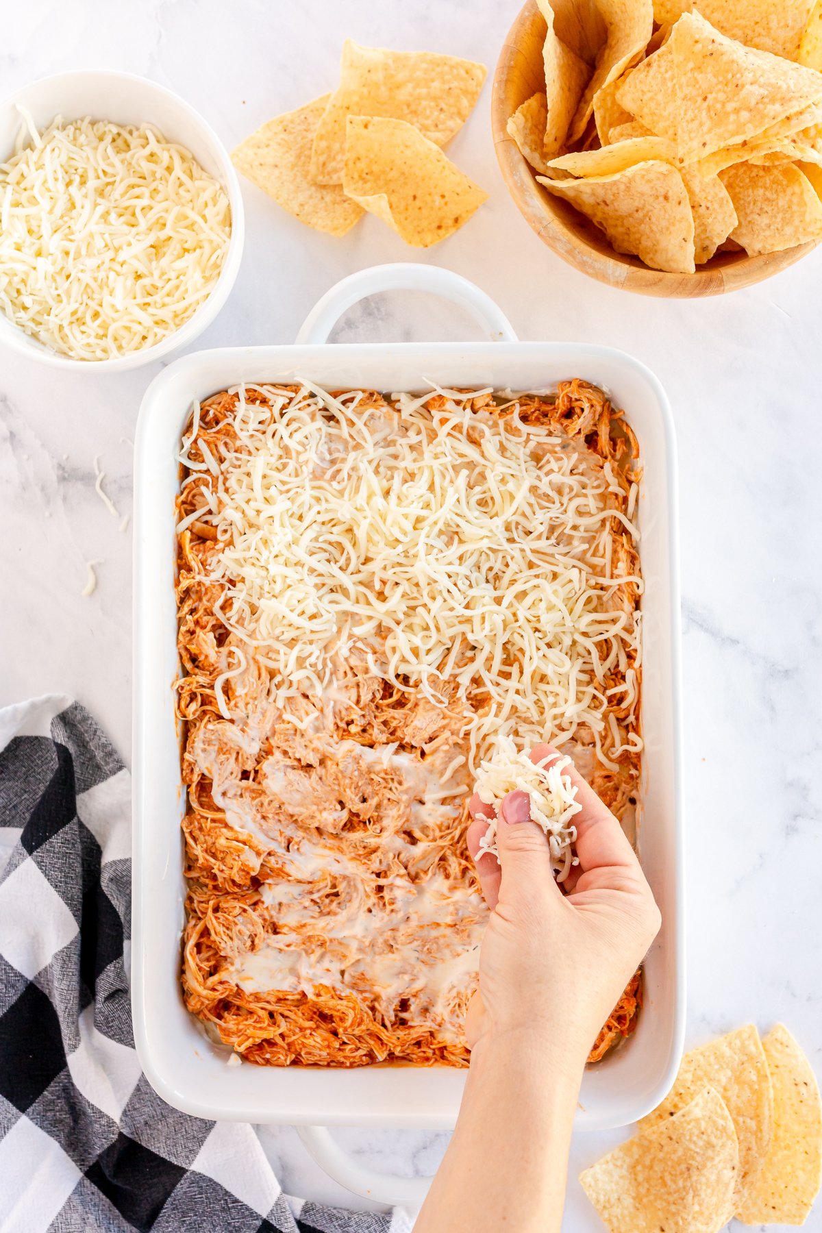 sprinkling shredded cheese on buffalo chicken dip