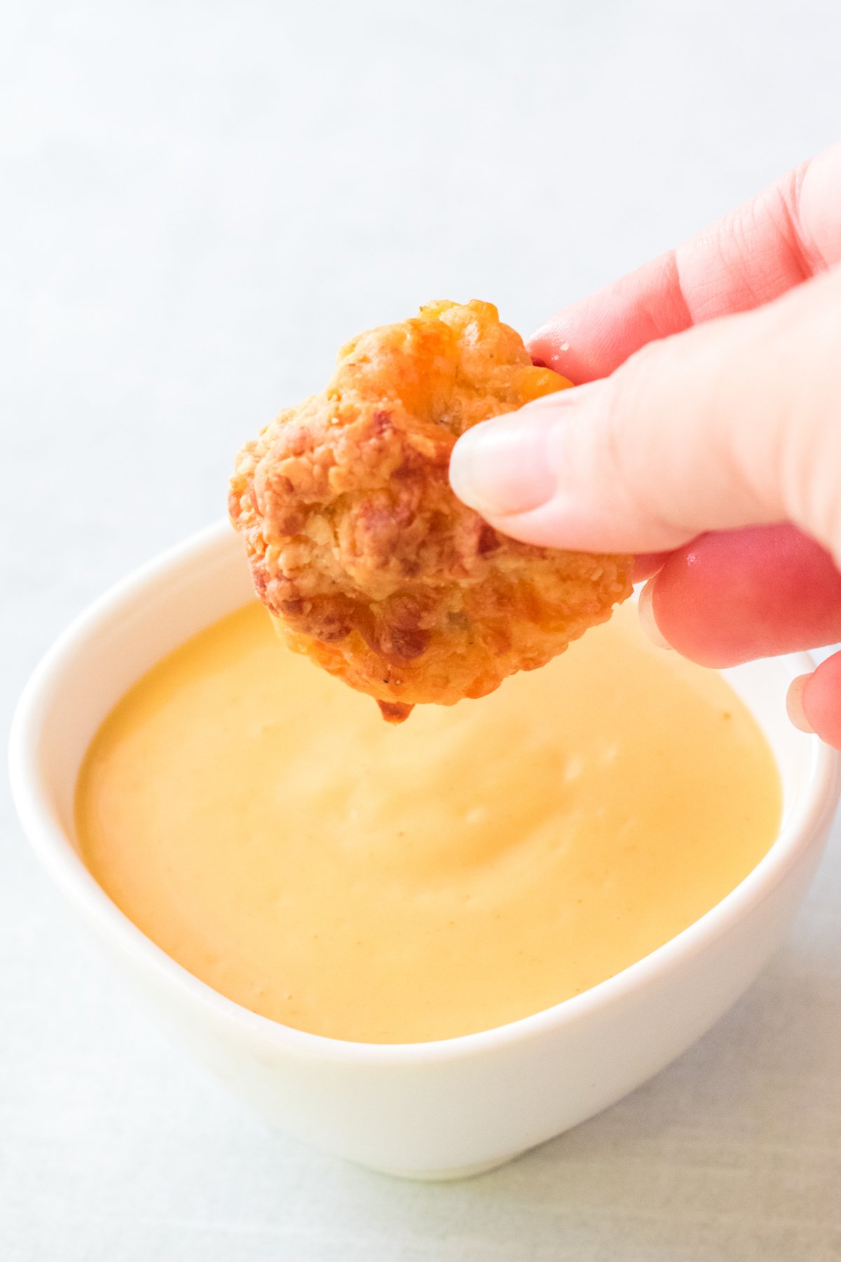 hand holding a sausage ball over honey mustard