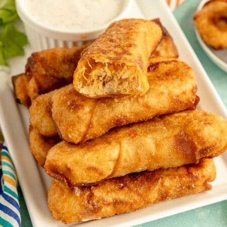 buffalo chicken egg rolls stacked on a white plate with ranch dressing