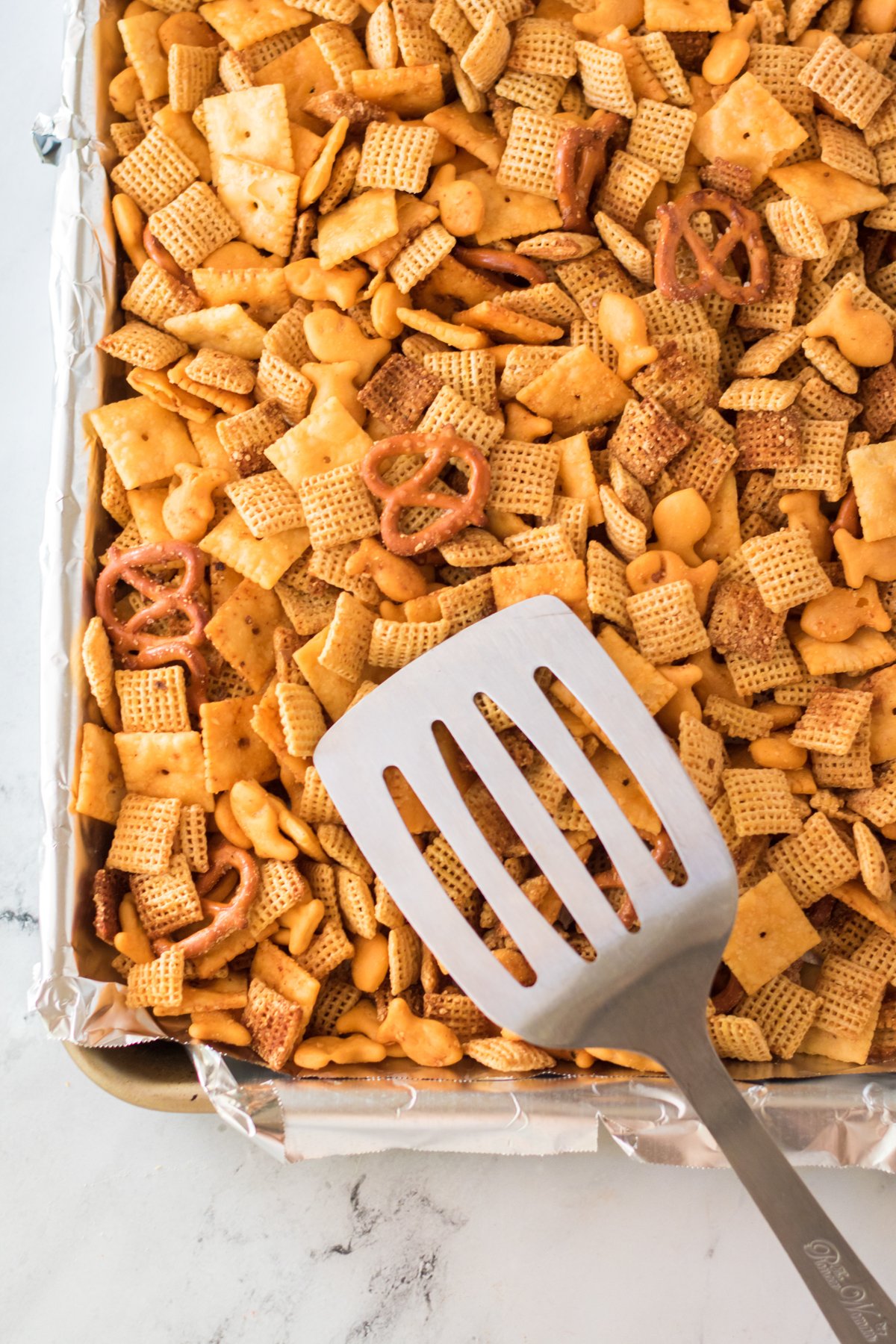 cheddar chex mix on baking sheets with a spatula