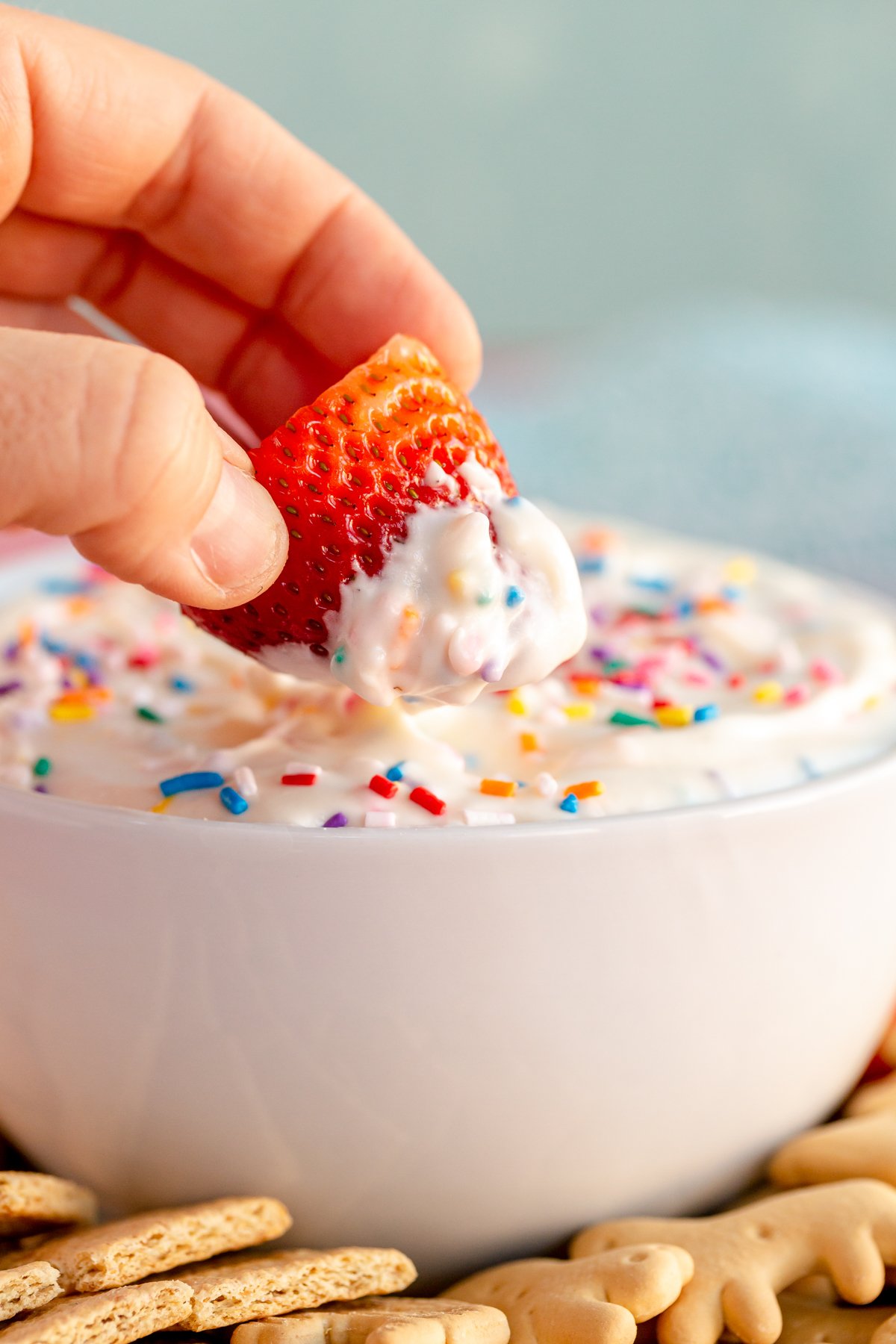 hand dipping strawberry into bowl of funfetti dip