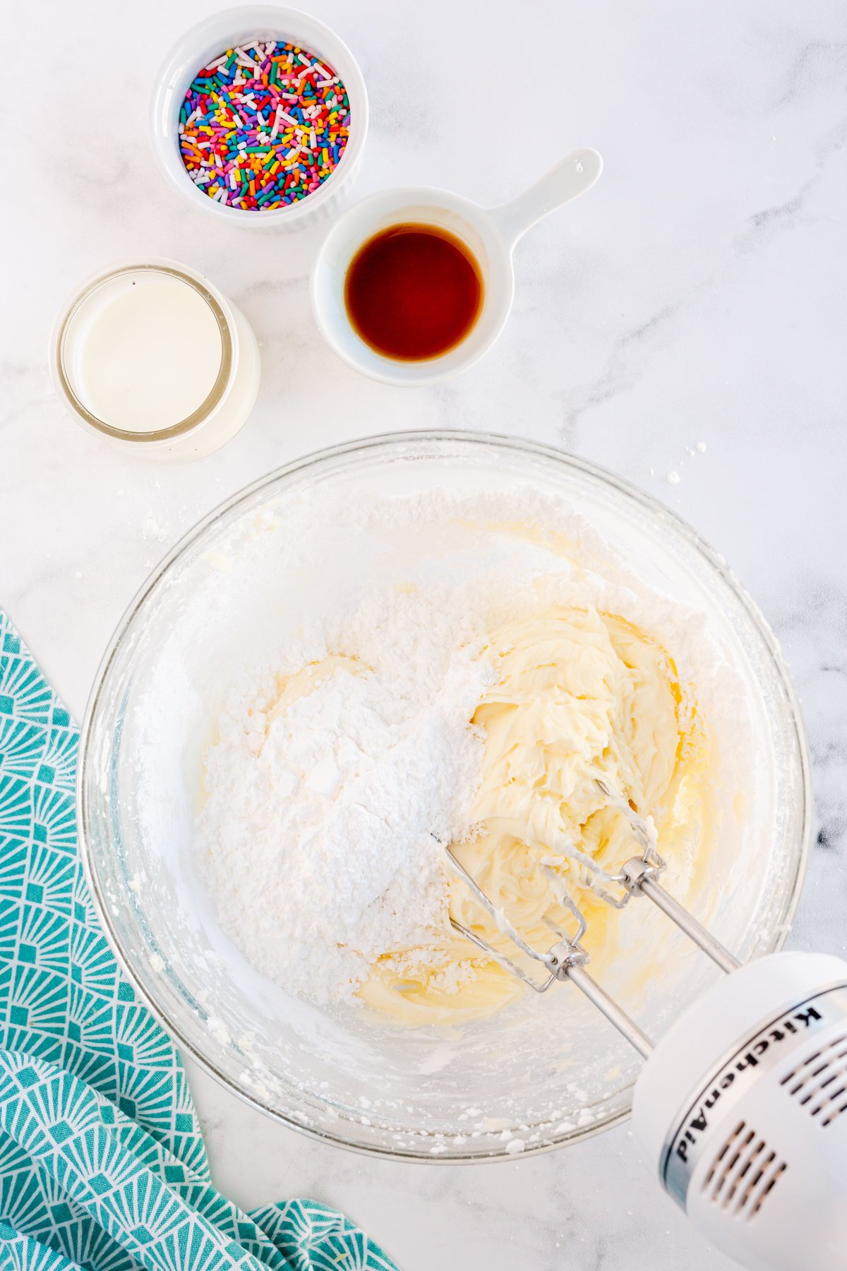 adding powdered sugar to a funfetti dip in a bowl