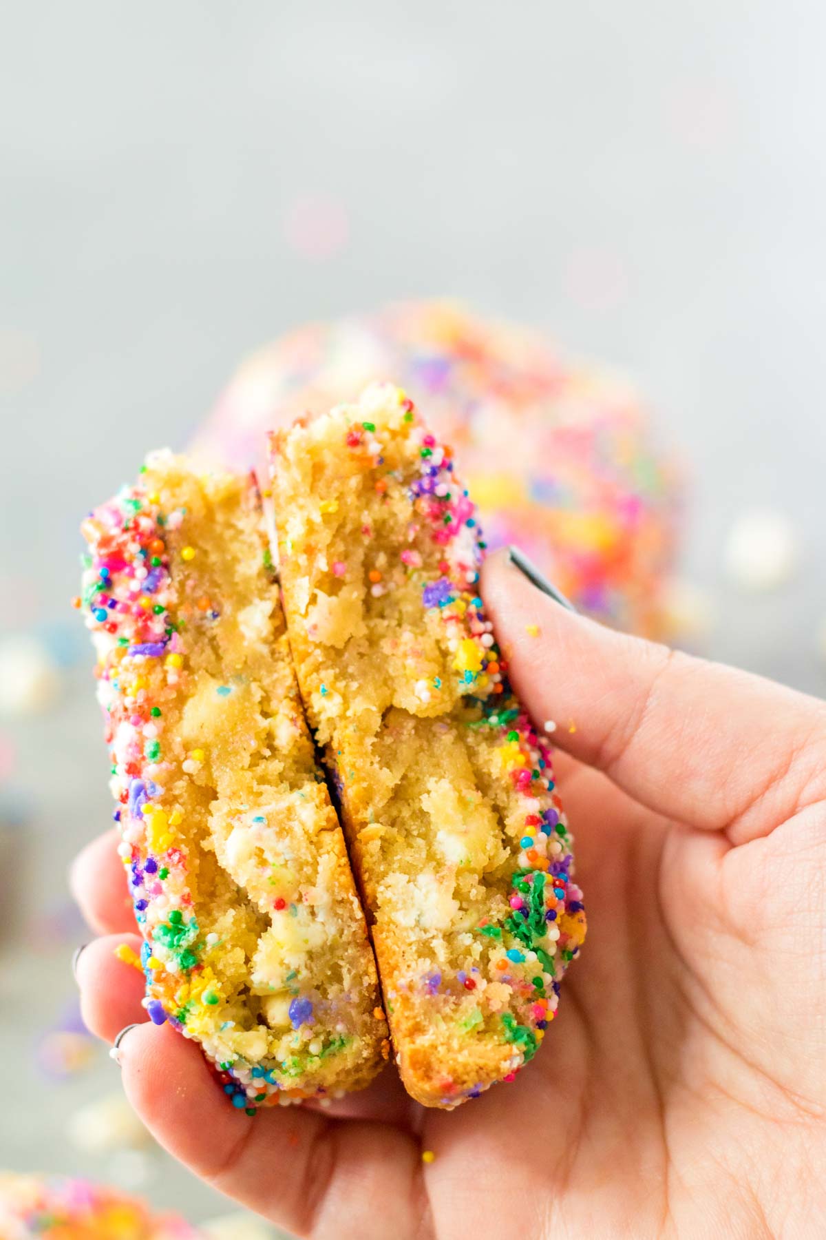 hand holding two halves of a sprinkle cookie