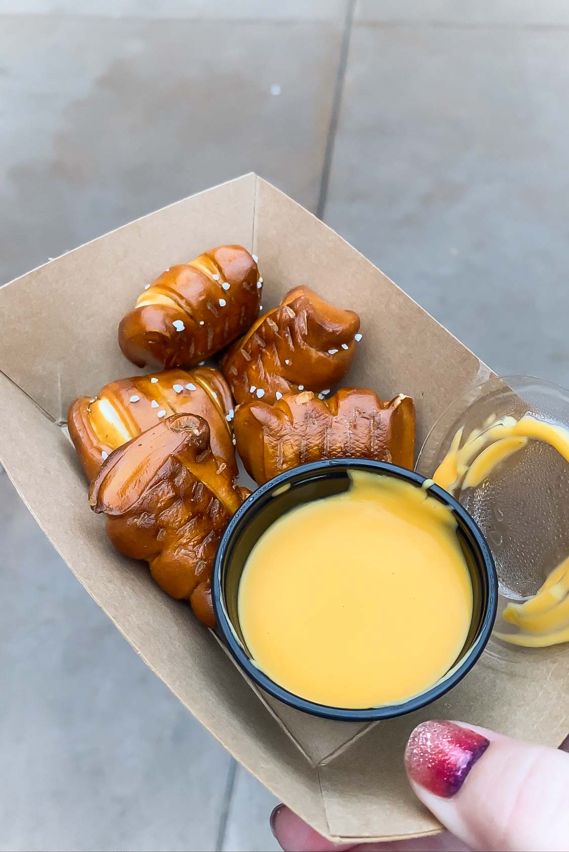 hand holding a tray with pretzel bites and dipping cheese