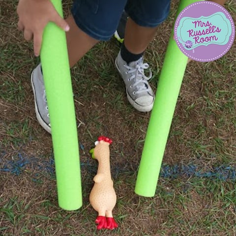 Kid trying to pick up a rubber chicken with pool noodles