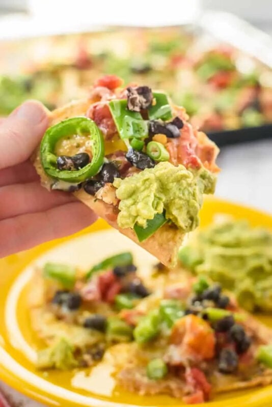 hand holding nachos above a plate of nachos