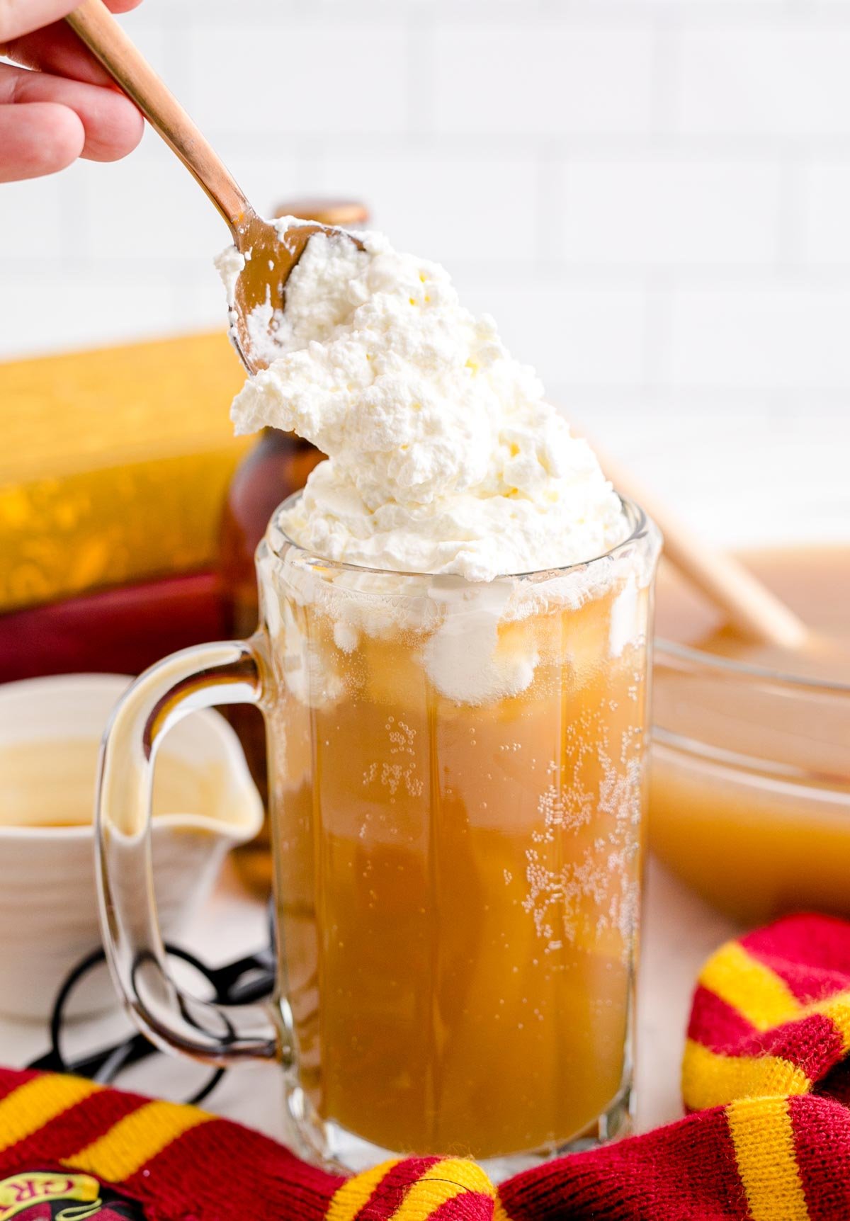 adding whipped cream to a glass of homemade butterbeer