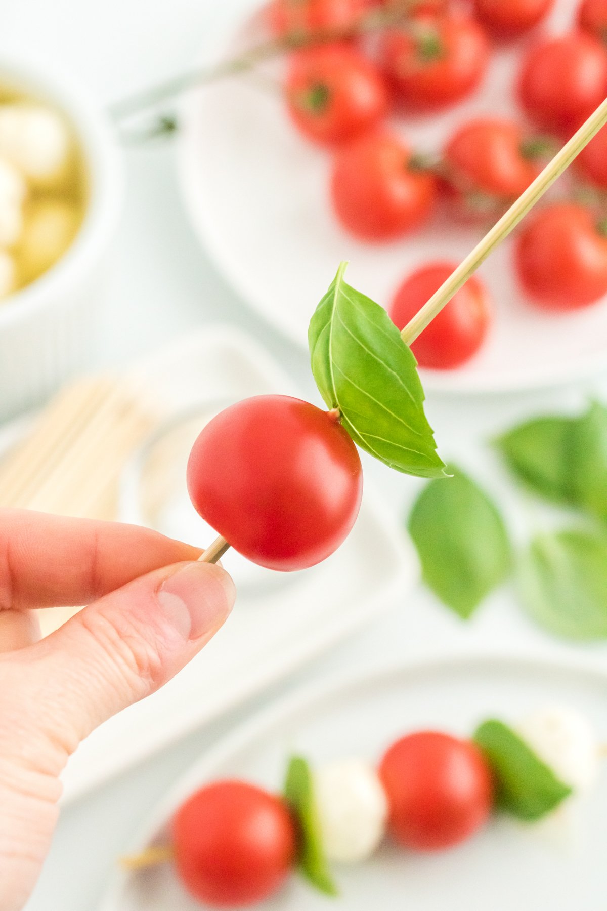 hand holding a skewer with a tomato and piece of basil