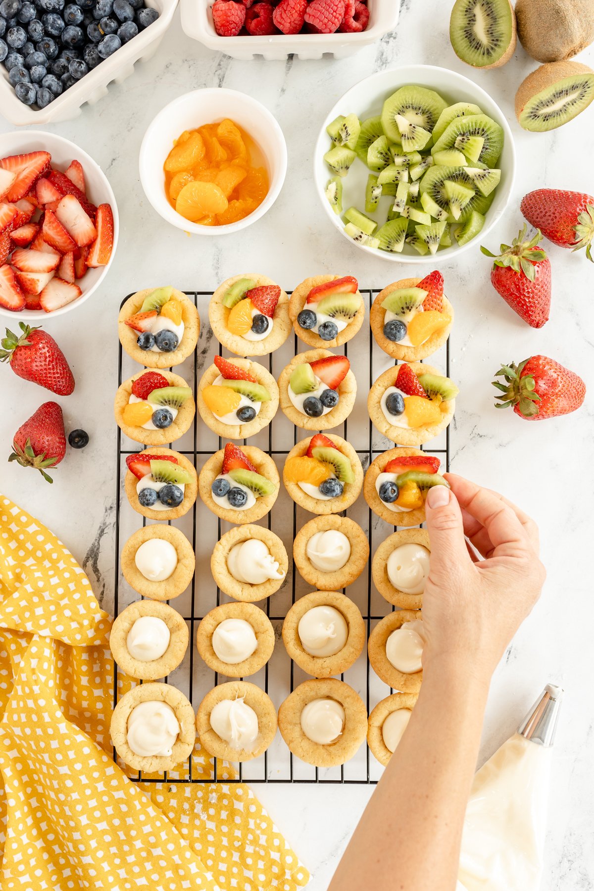 hand placing fruit on top of mini fruit tarts