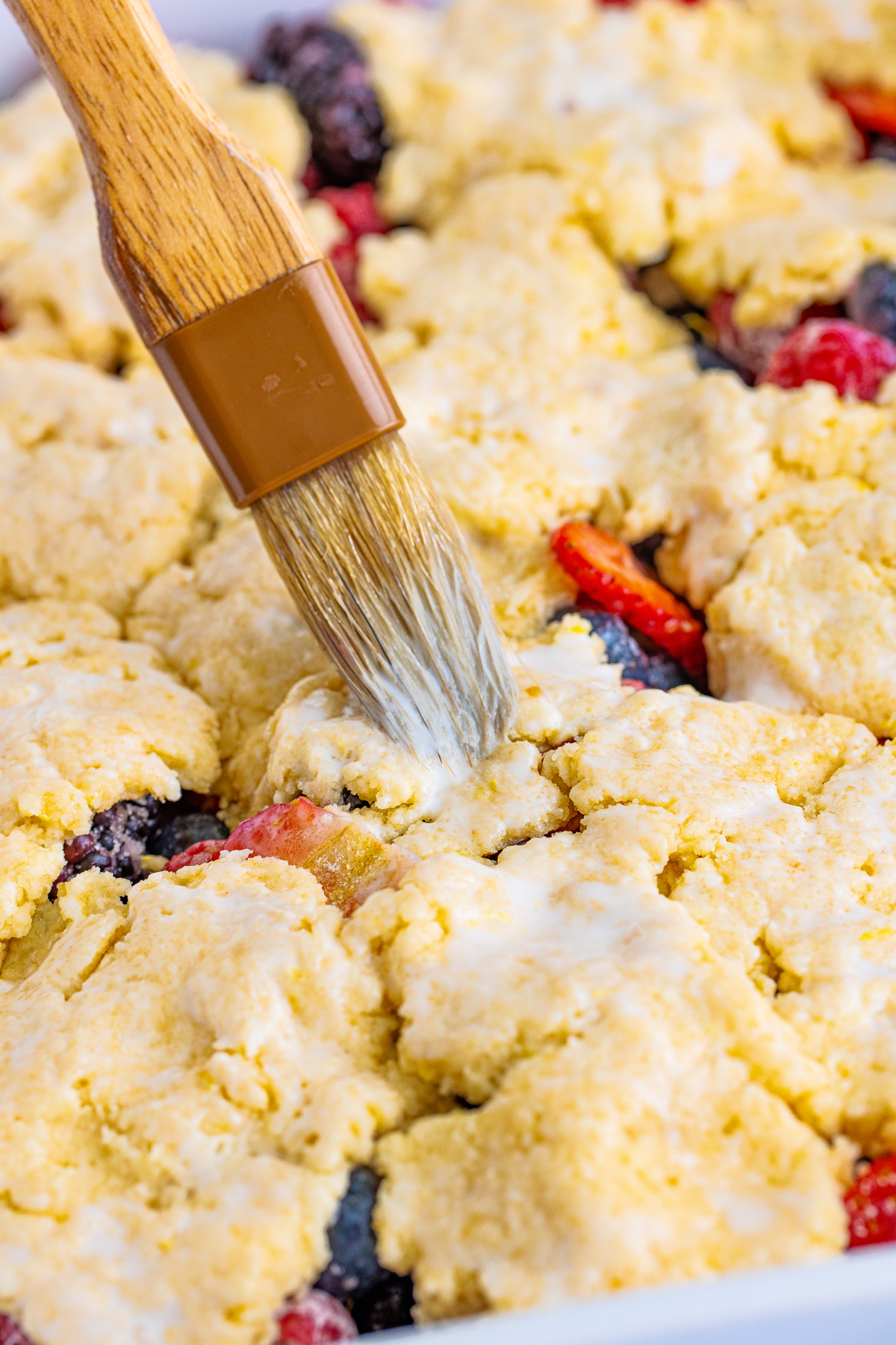 brushing mixed berry cobbler topping with a pastry brush