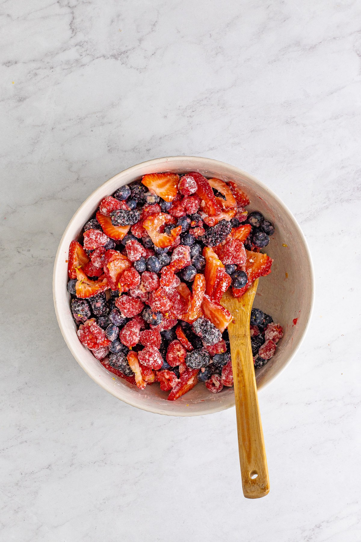 wooden spoon in a white bowl full of mixer berries