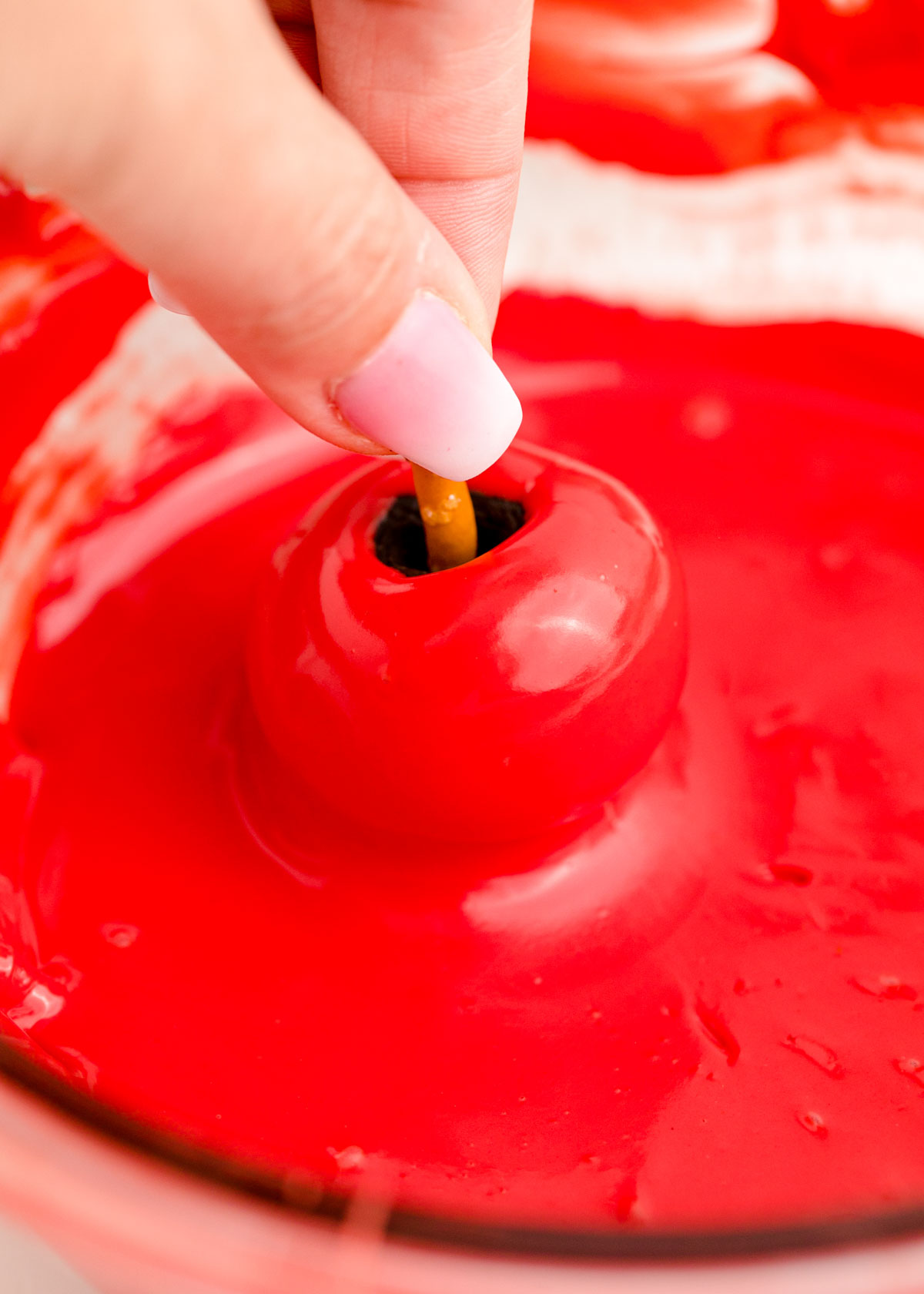 Hand dipping Oreo balls into red candy melts