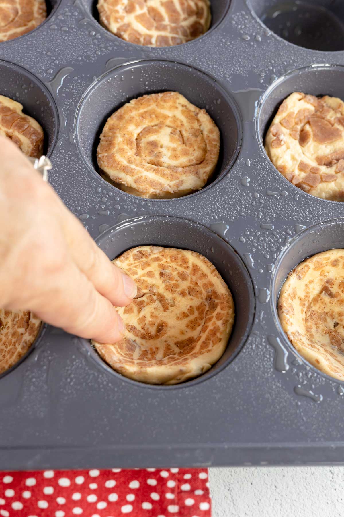 hand pressing cinnamon roll into a muffin tin