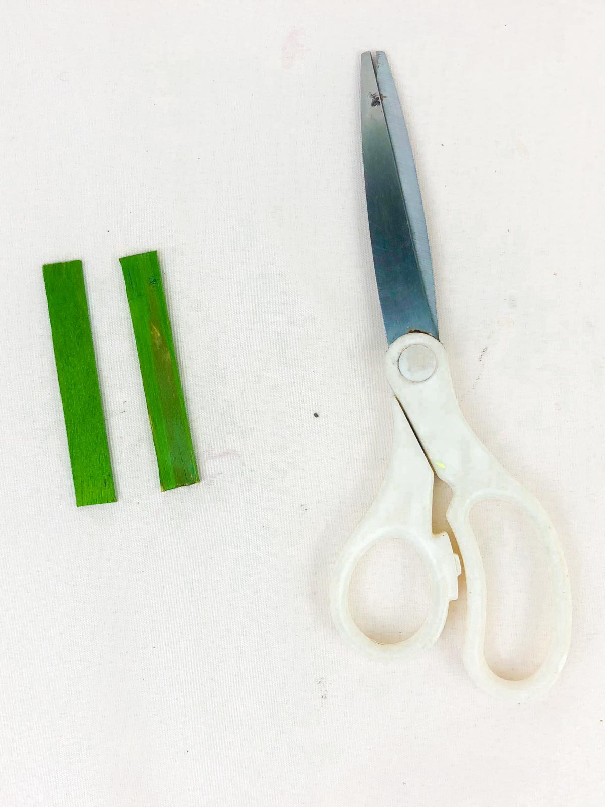 two pieces of green popsicle sticks with a pair of scissors
