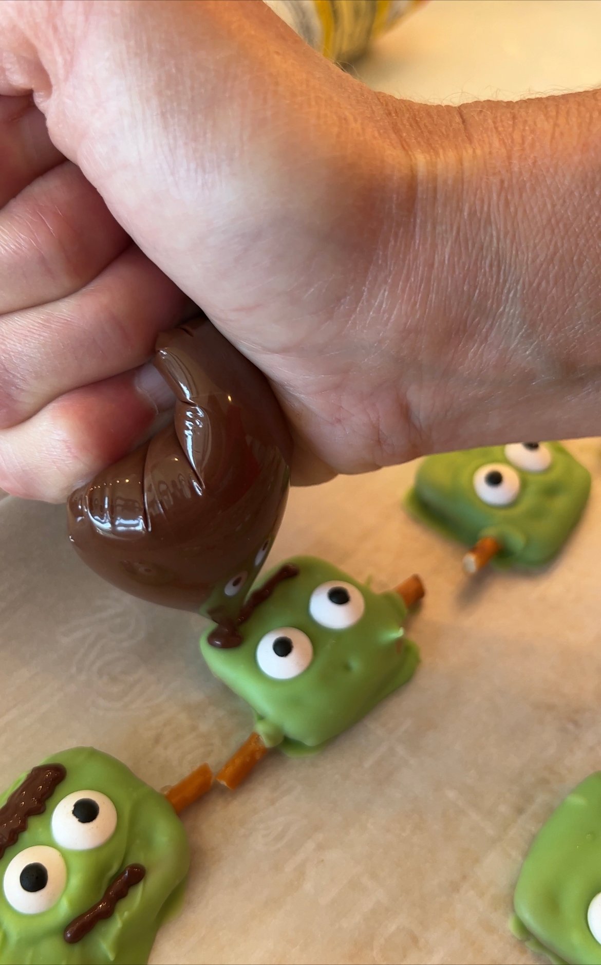 hand using a piping bag to decorate Halloween pretzels with chocolate